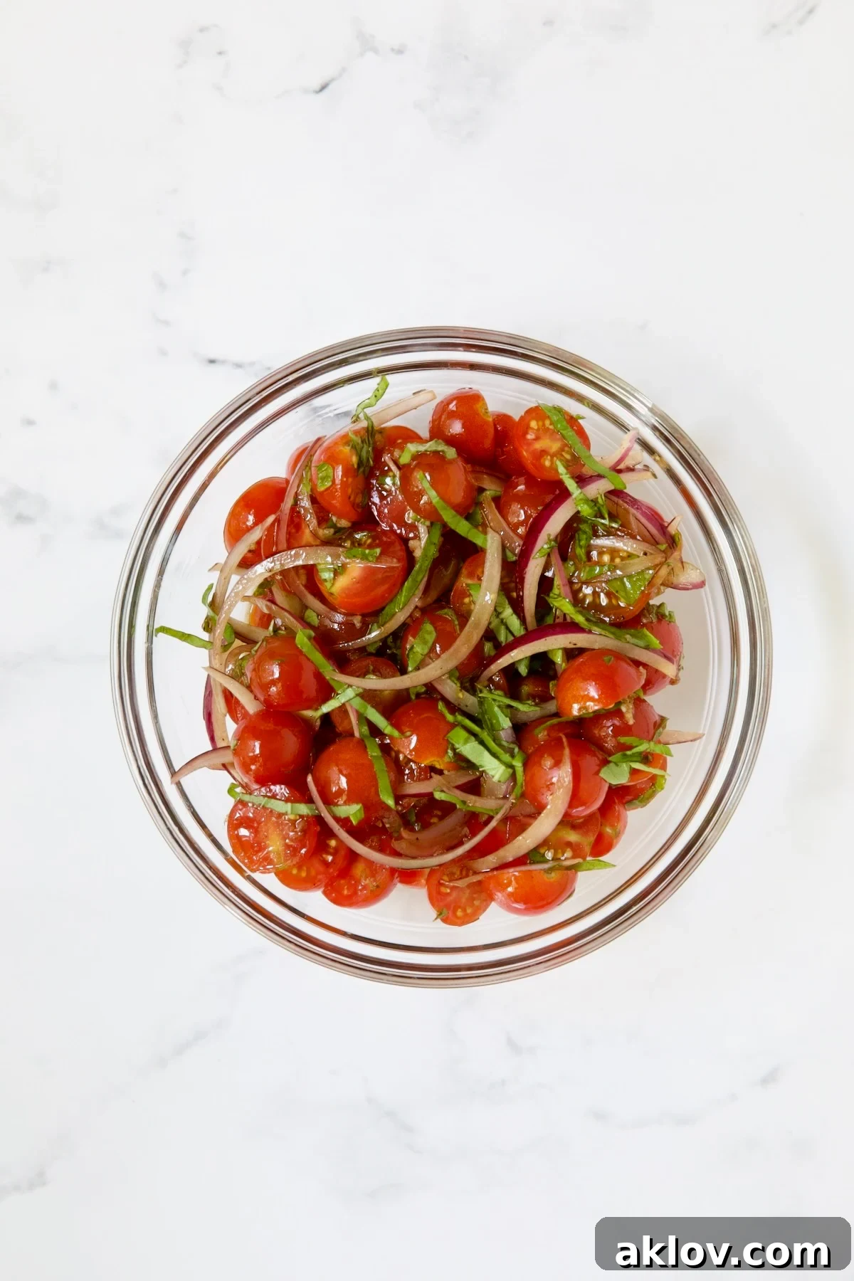 Golden Crispy Milanese 6 A vibrant cherry tomato salad with red onion, garlic, and basil in a clear glass bowl, marinating.