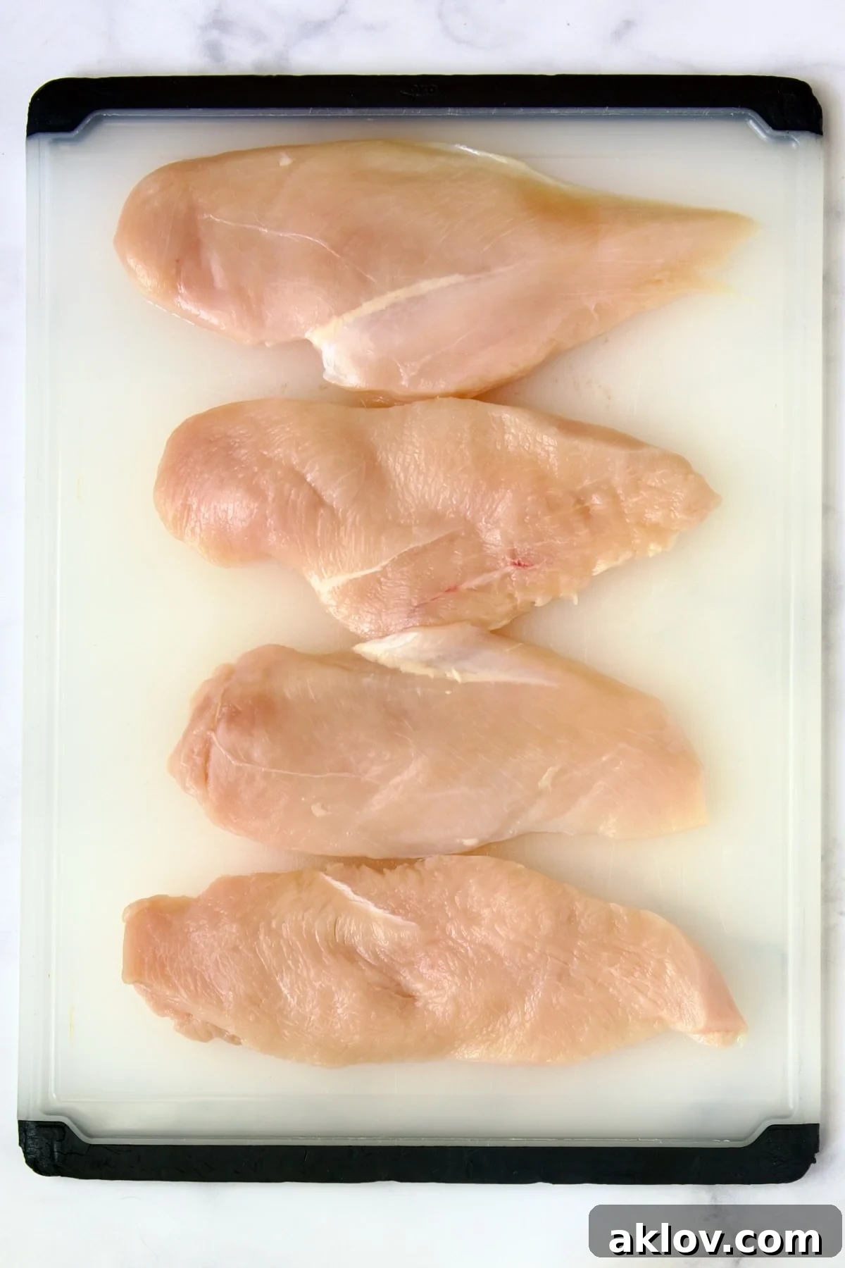 Golden Crispy Milanese 7 Four perfectly portioned and pounded raw chicken cutlets arranged neatly on a white plastic cutting board, ready for breading.