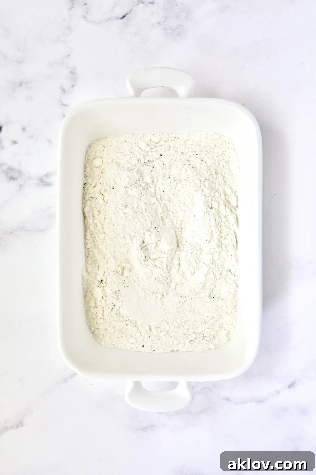 Golden Crispy Milanese 8 A white dish filled with seasoned all-purpose flour, ready for the first step of breading.