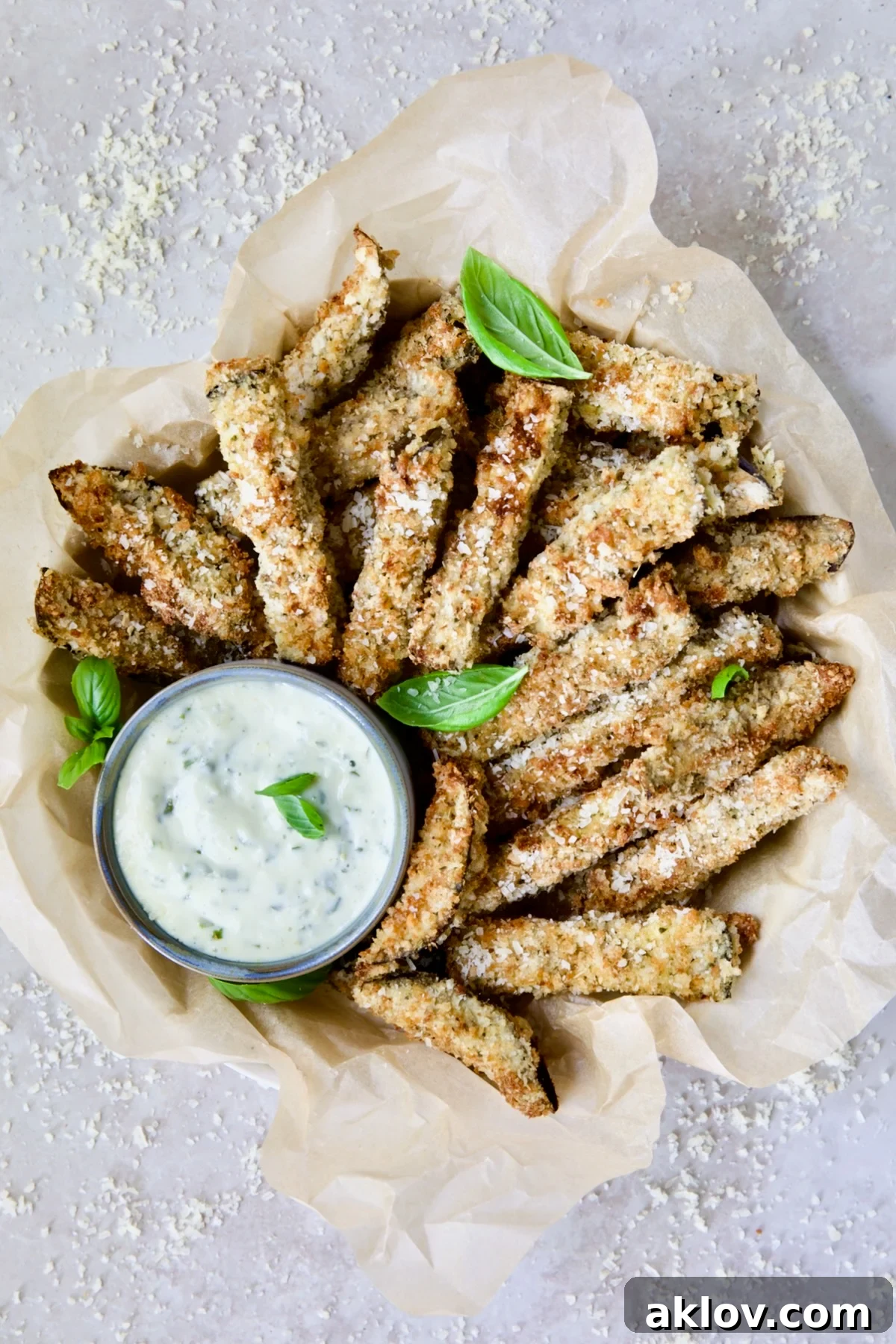 Air Fryer Eggplant Fries with Garlic Basil Aioli in basket with parmesan cheese and fresh basil leaves.
