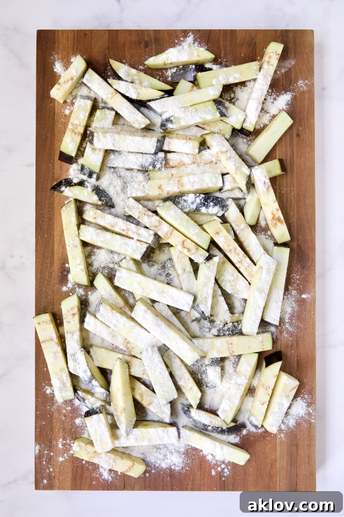 Eggplant fries on wood cutting board dusted with all-purpose flour.