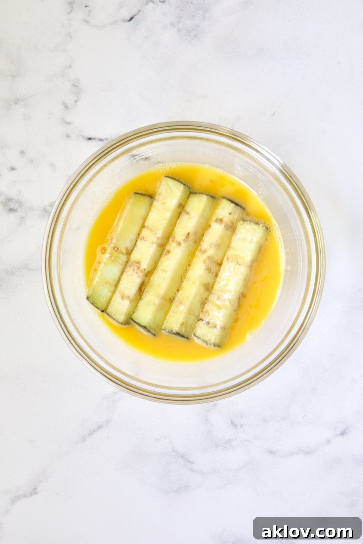 Eggplant fries in beaten egg in glass bowl.