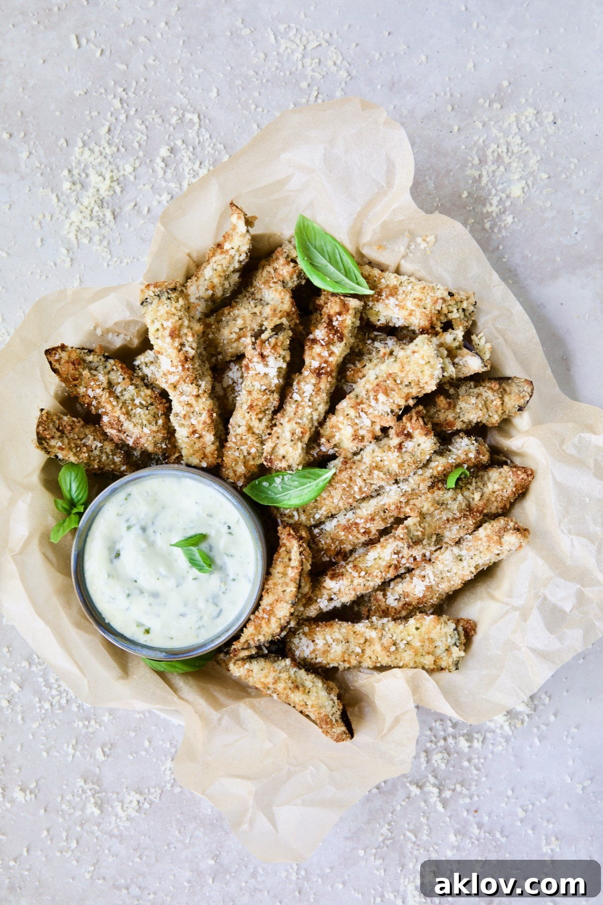 Air Fryer Eggplant Fries with Garlic Basil Aioli in parchment paper lined basket with Parmesan cheese scattered about.