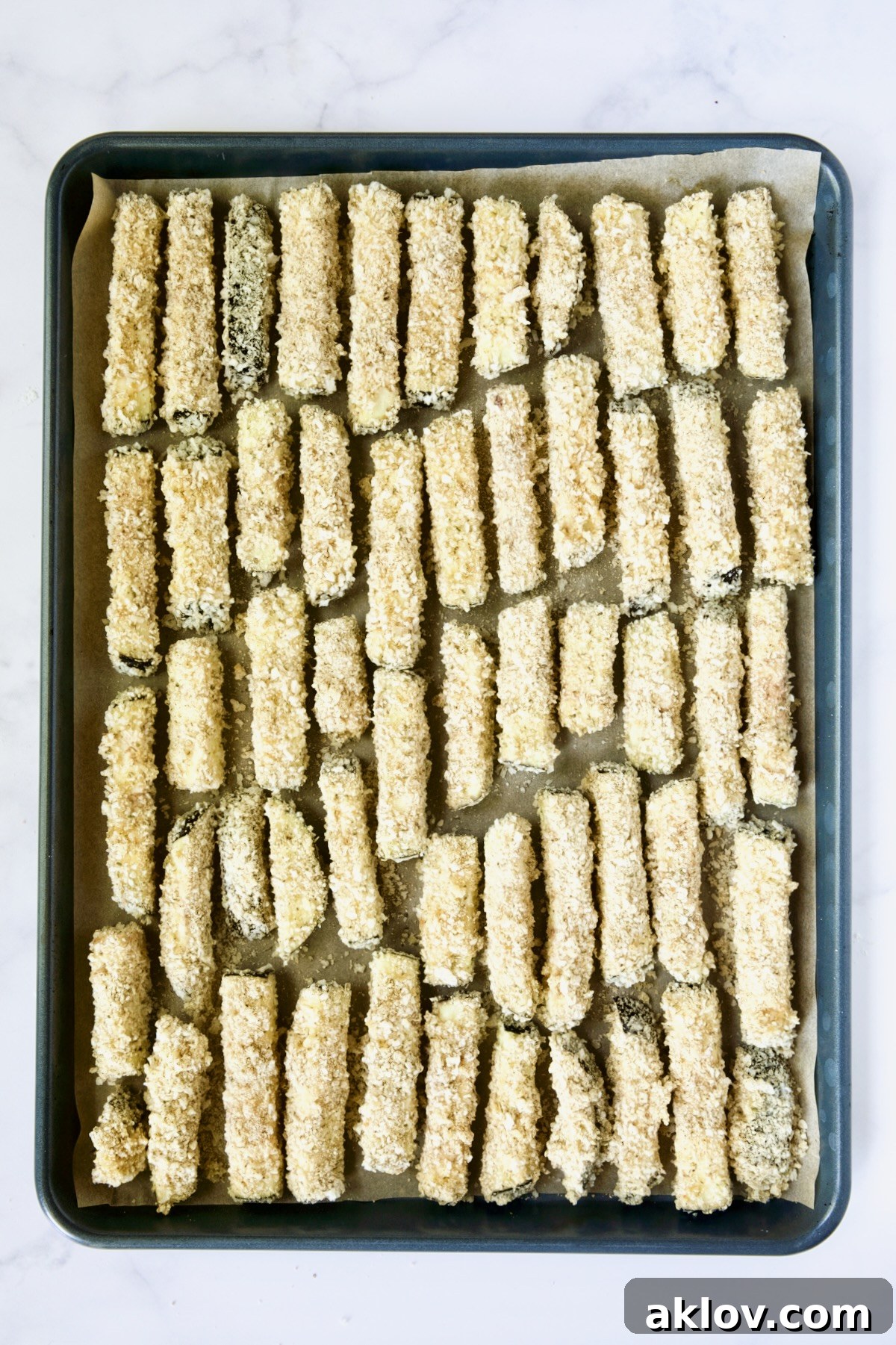 Breaded eggplant fries on parchment paper-lined rimmed baking sheet.