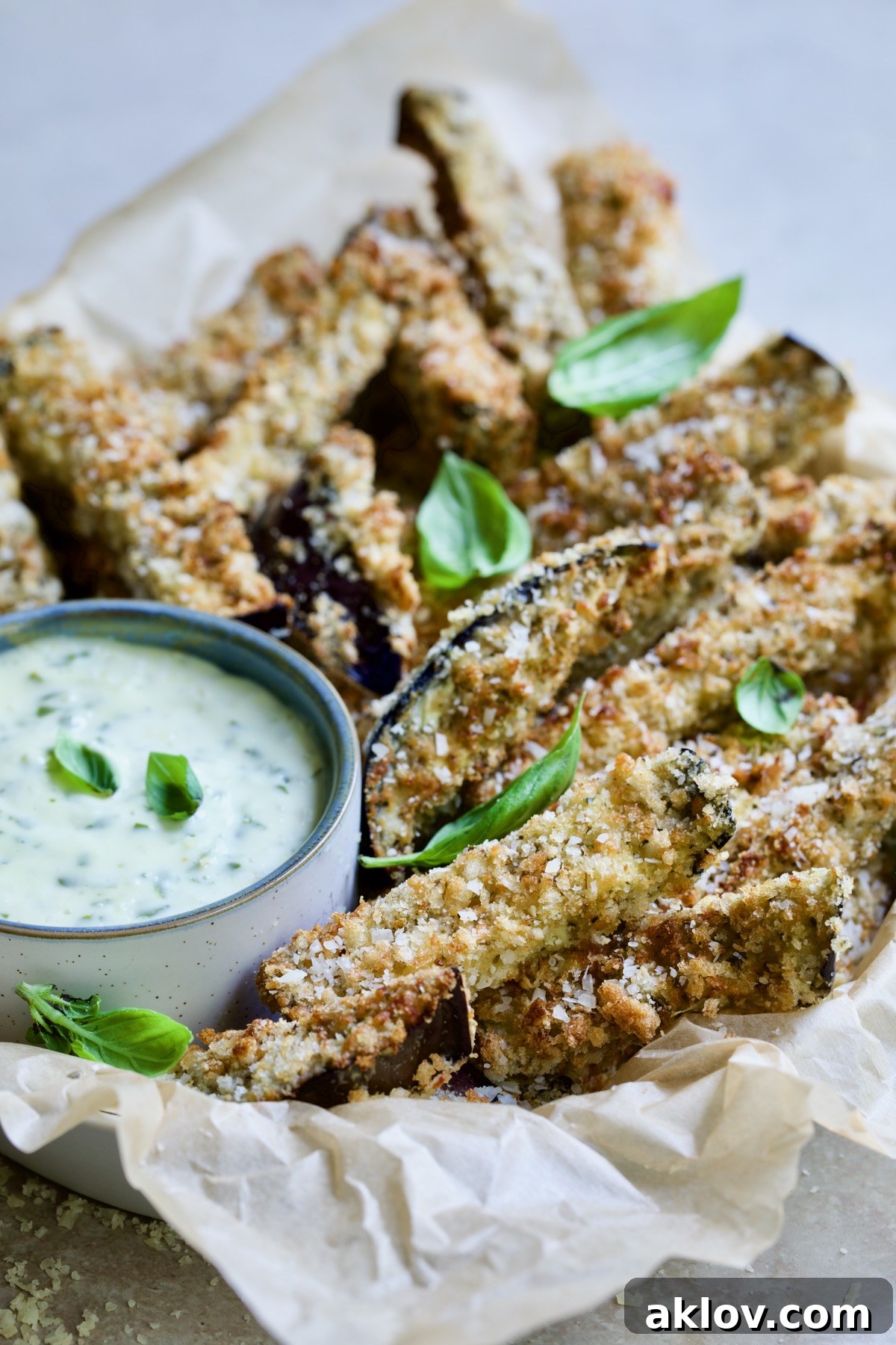 Air Fryer Eggplant Fries with Garlic Basil Aioli in parchment lined basket garnished with fresh basil.