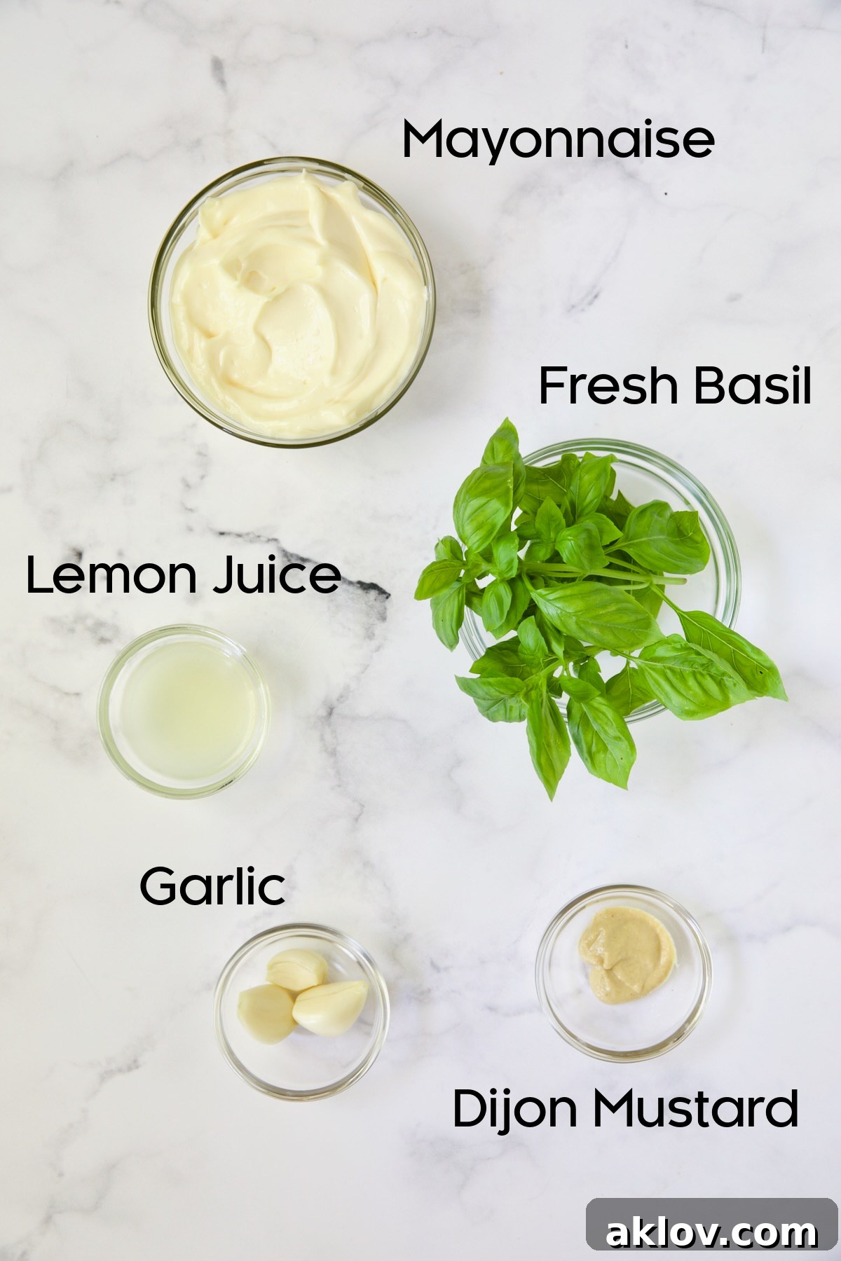 Ingredients for Garlic Basil Aioli in glass bowls on white background.