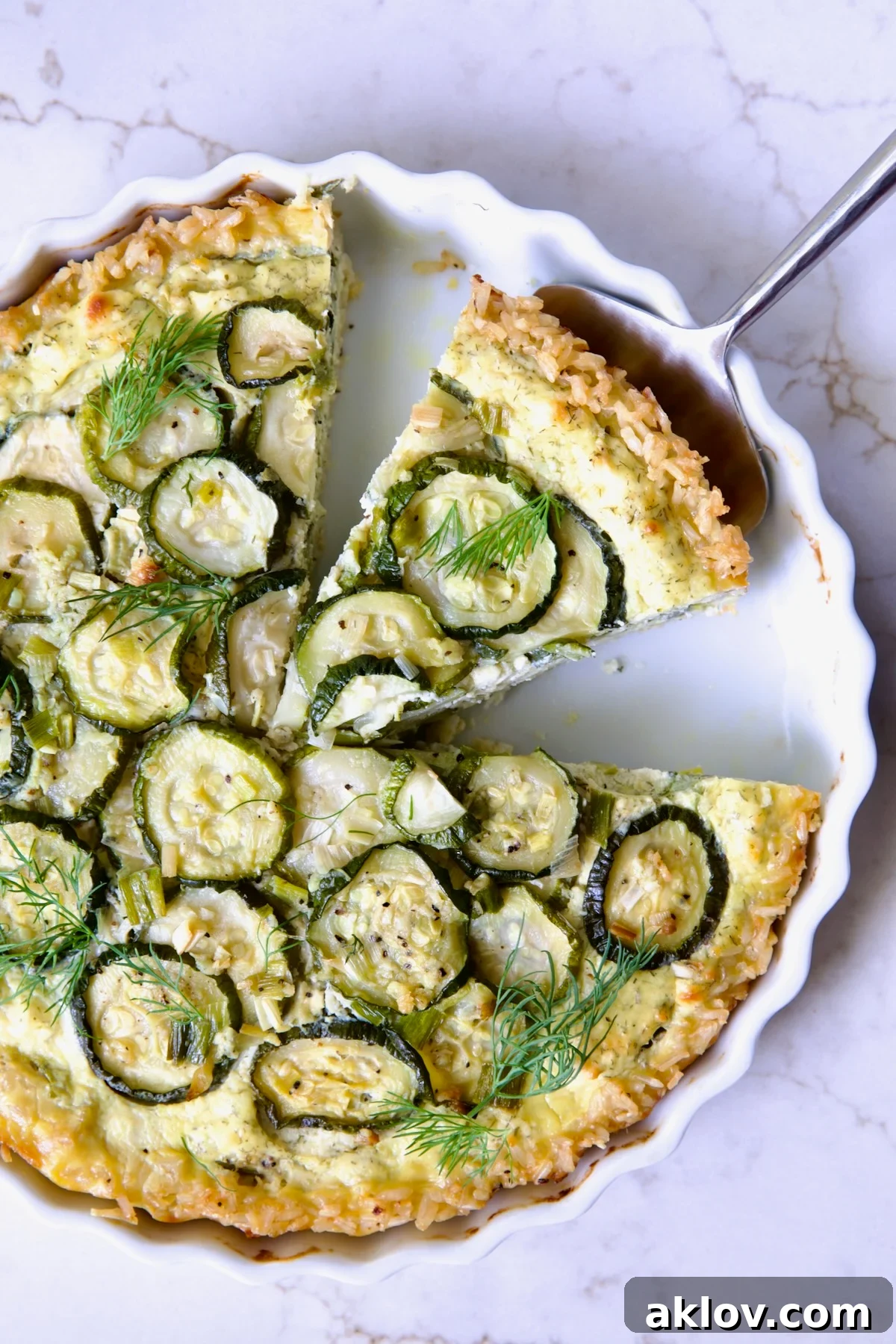 Zucchini Quiche in white quiche dish with pie server picking up a piece.