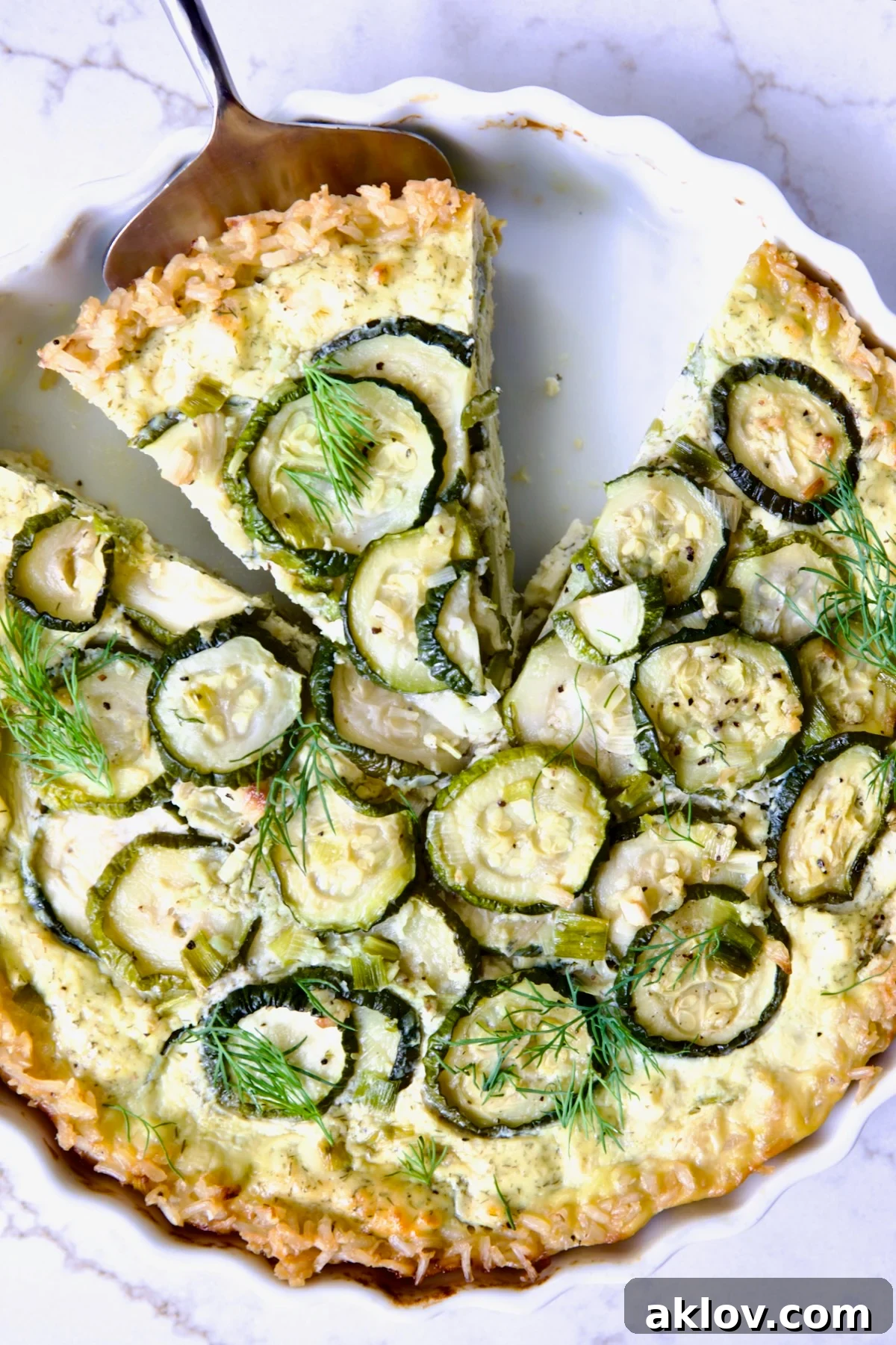 Zucchini Quiche in white quiche dish with pie server picking up a piece.