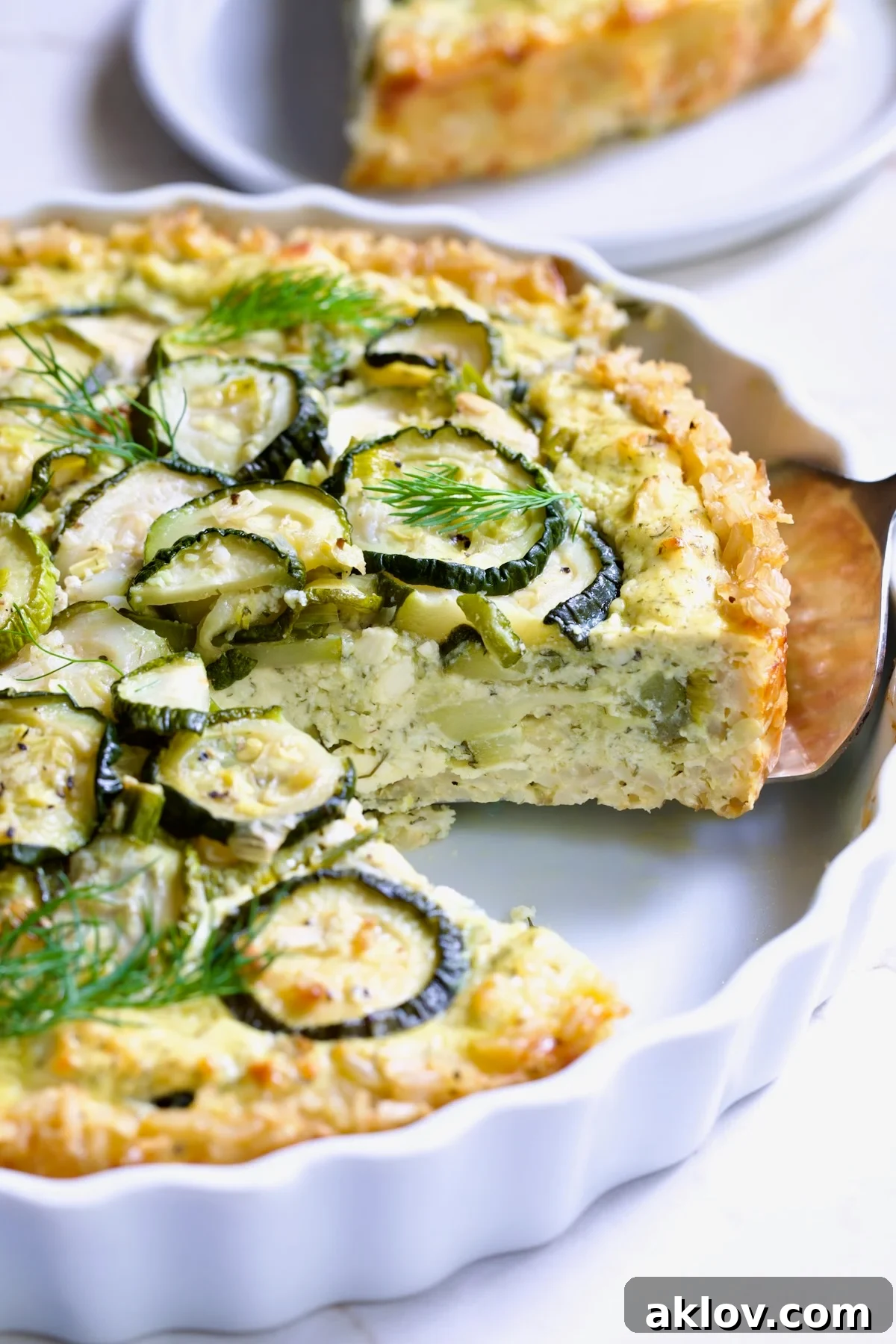 Zucchini Quiche in white quiche dish with pie server picking up a piece.