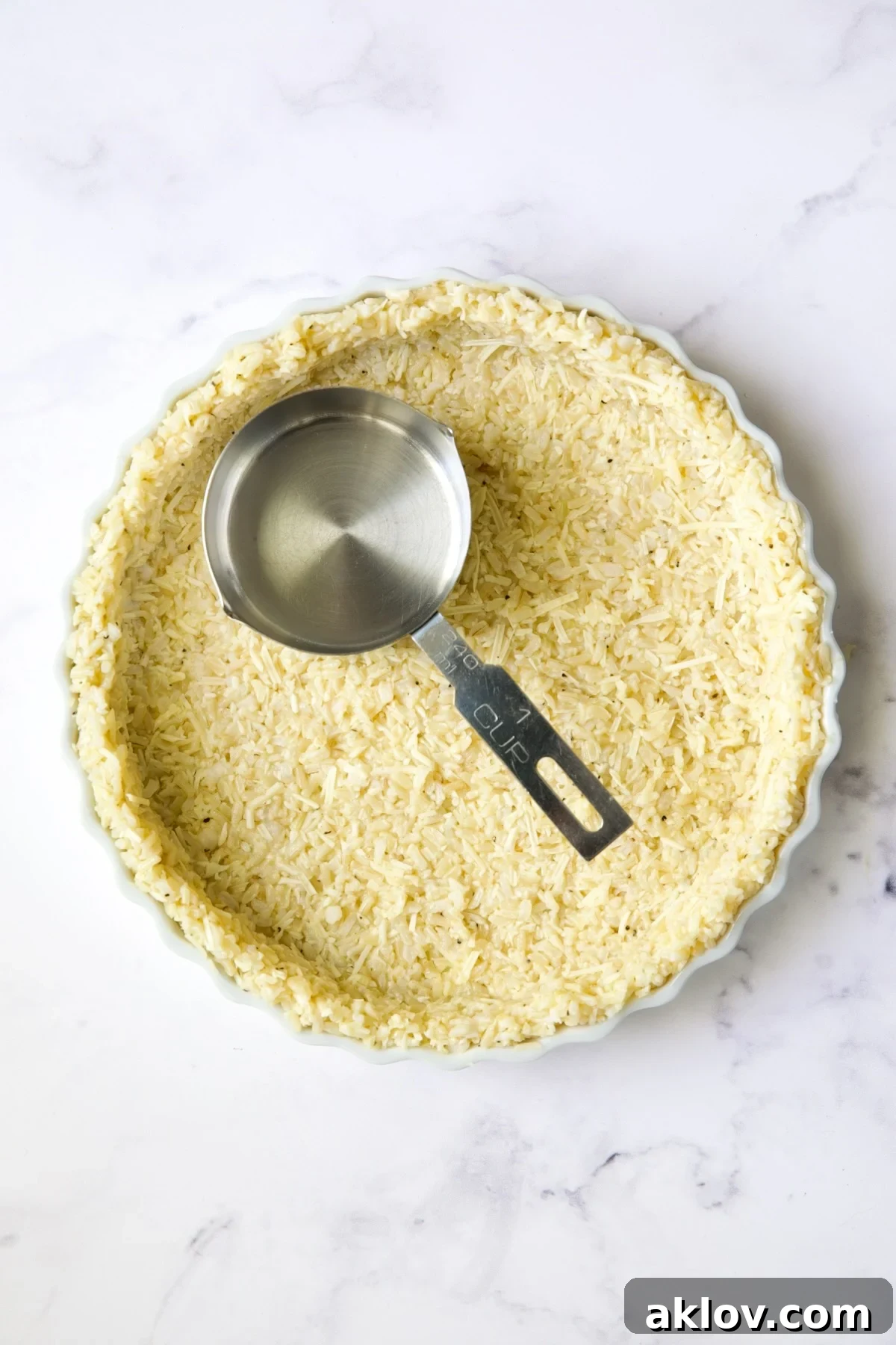 Unbaked brown rice crust with 1-cup measuring cup pressing crust.