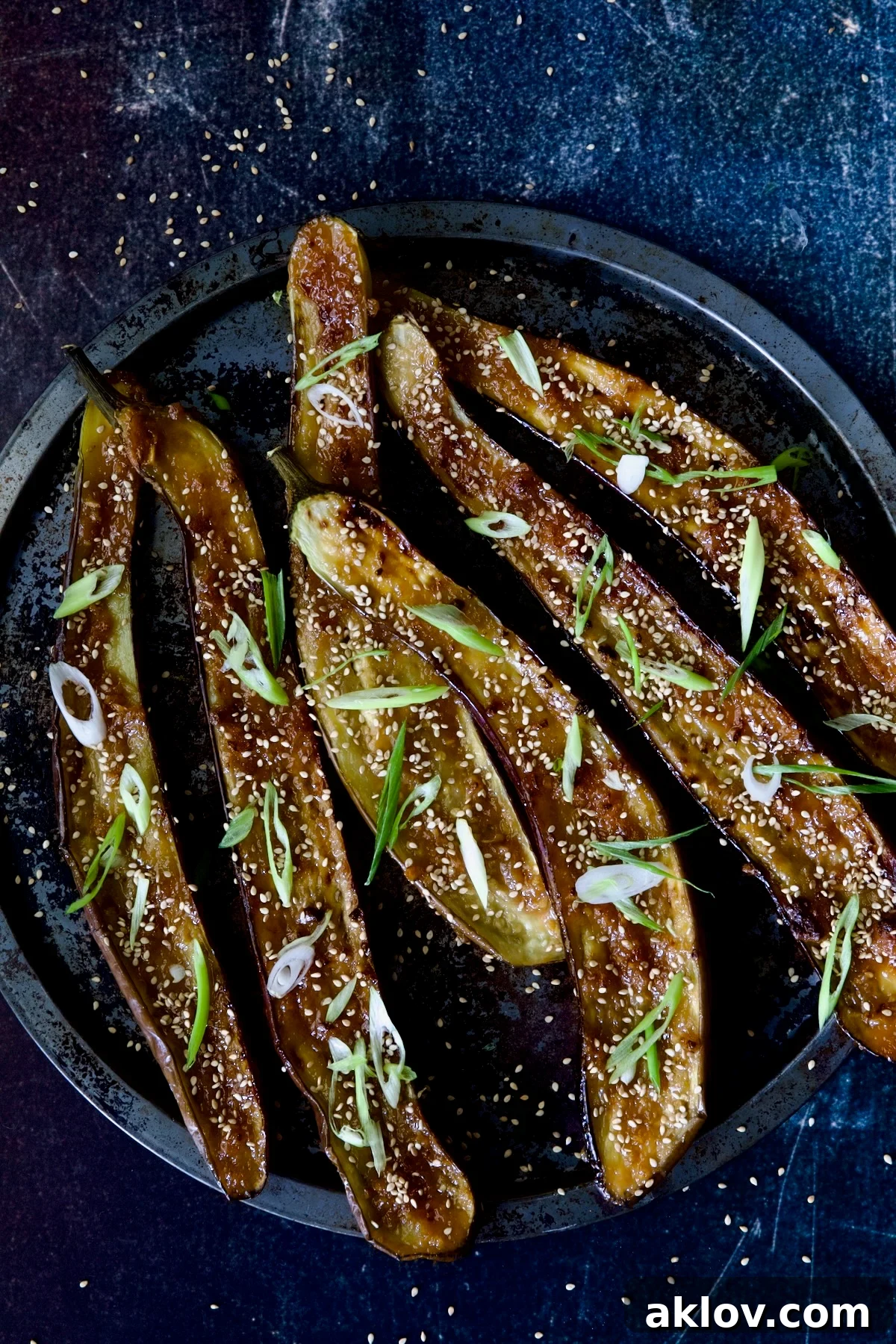 Six Miso-Glazed Japanese Eggplant halves on a metal baking tray, beautifully garnished with toasted sesame seeds and finely chopped scallions.