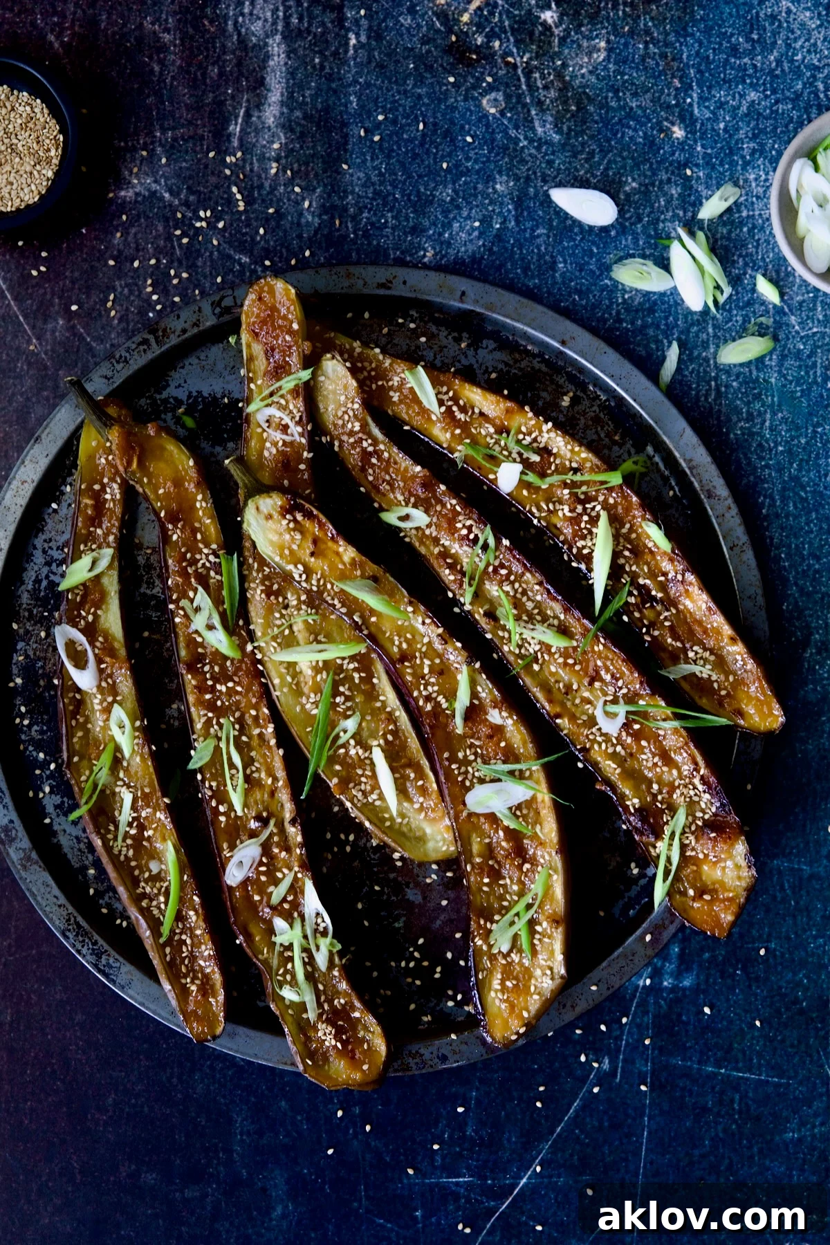 Miso-Glazed Eggplant garnished generously with vibrant green scallions and toasted sesame seeds, scattered across the dish for an appealing presentation.