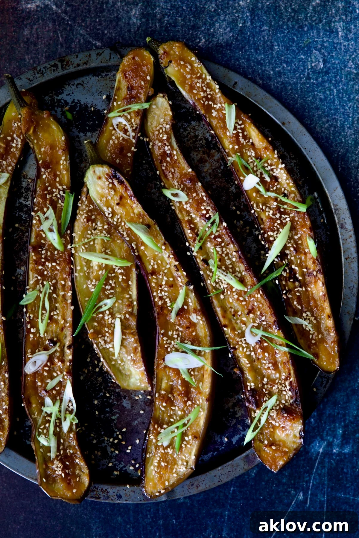 A beautifully presented Miso-Glazed Eggplant on a rustic round metal pan, garnished with freshly chopped scallions and a sprinkle of sesame seeds.