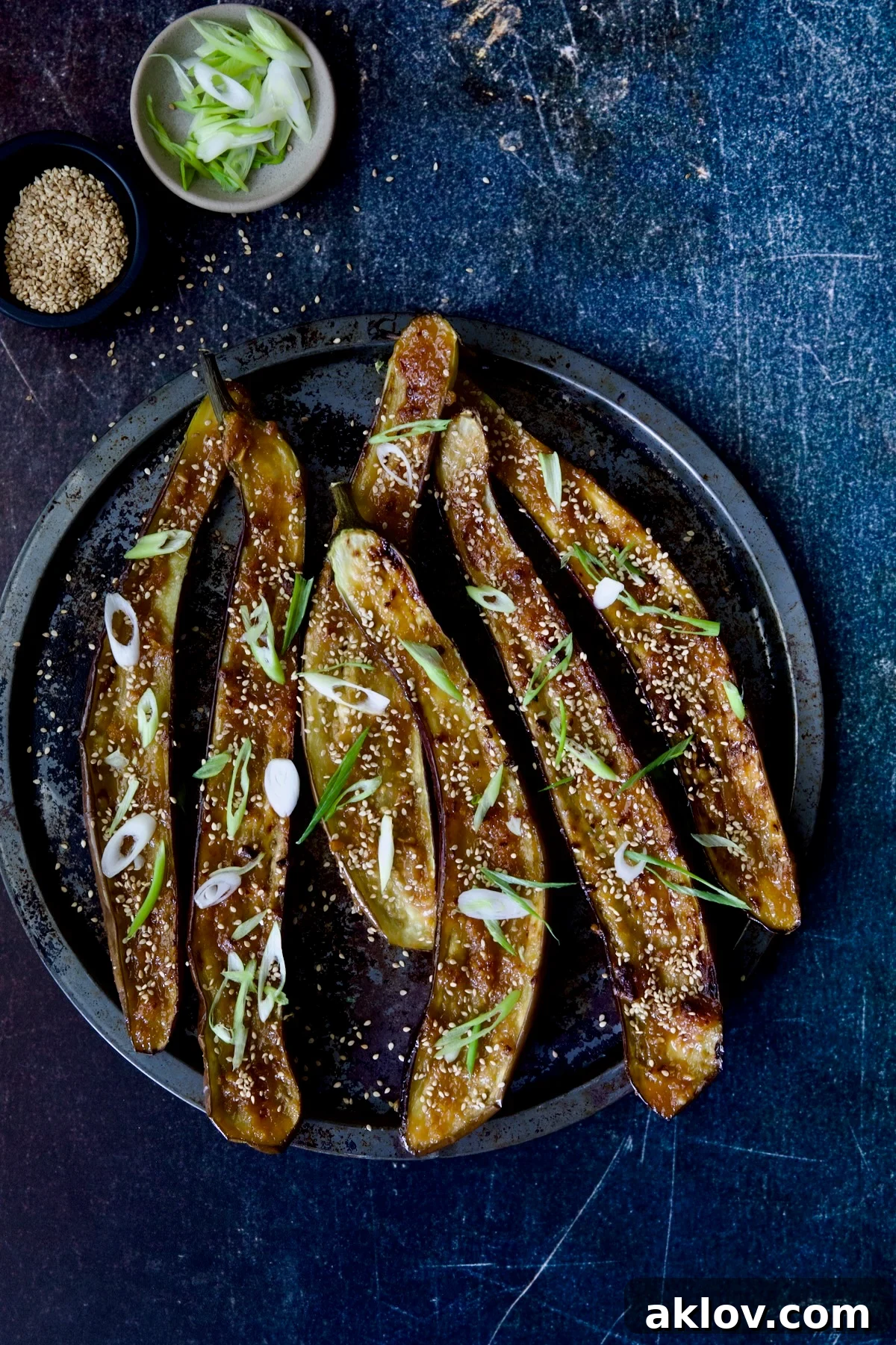 Close-up of perfectly broiled Miso-Glazed Eggplant on a metal tray, sprinkled with fresh scallions and sesame seeds, showcasing the caramelized glaze.