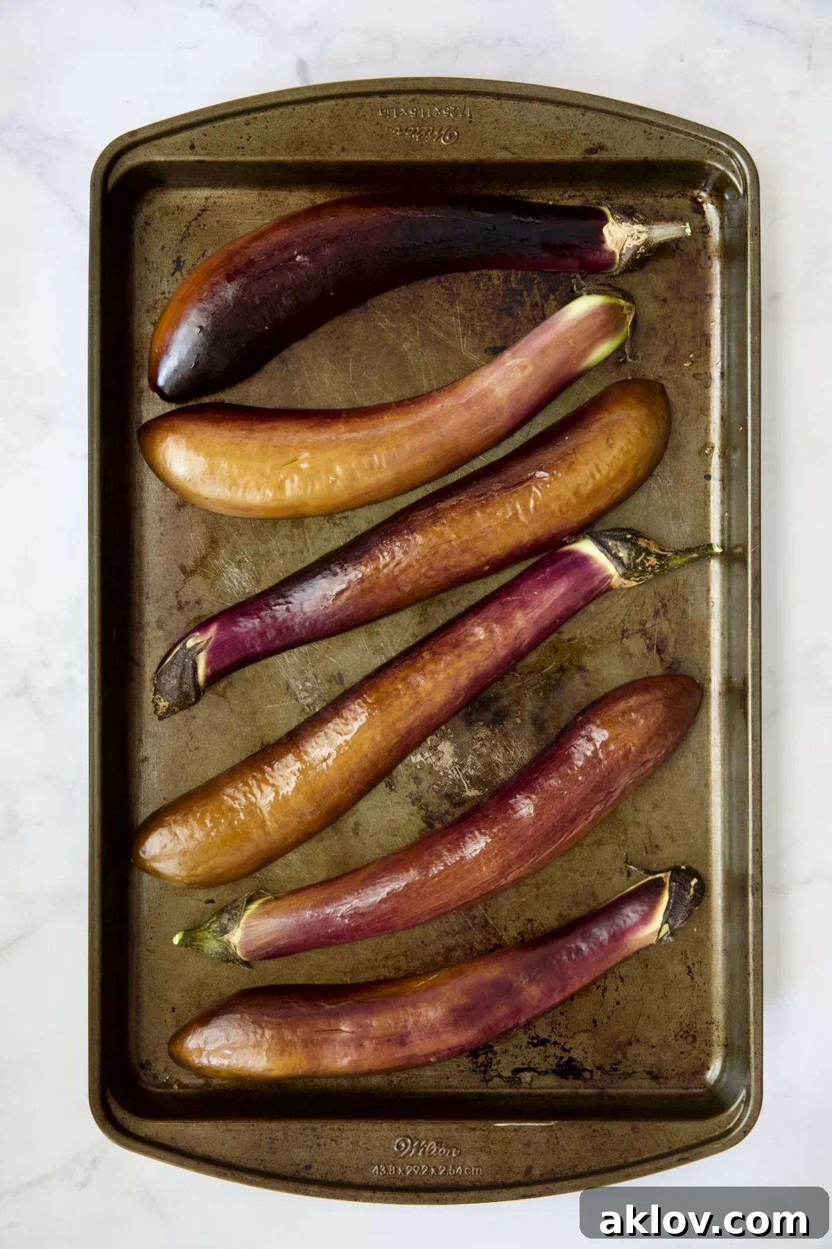 Six baked Japanese eggplant halves, now tender and slightly shrunken, resting on a rimmed baking sheet after their initial bake.