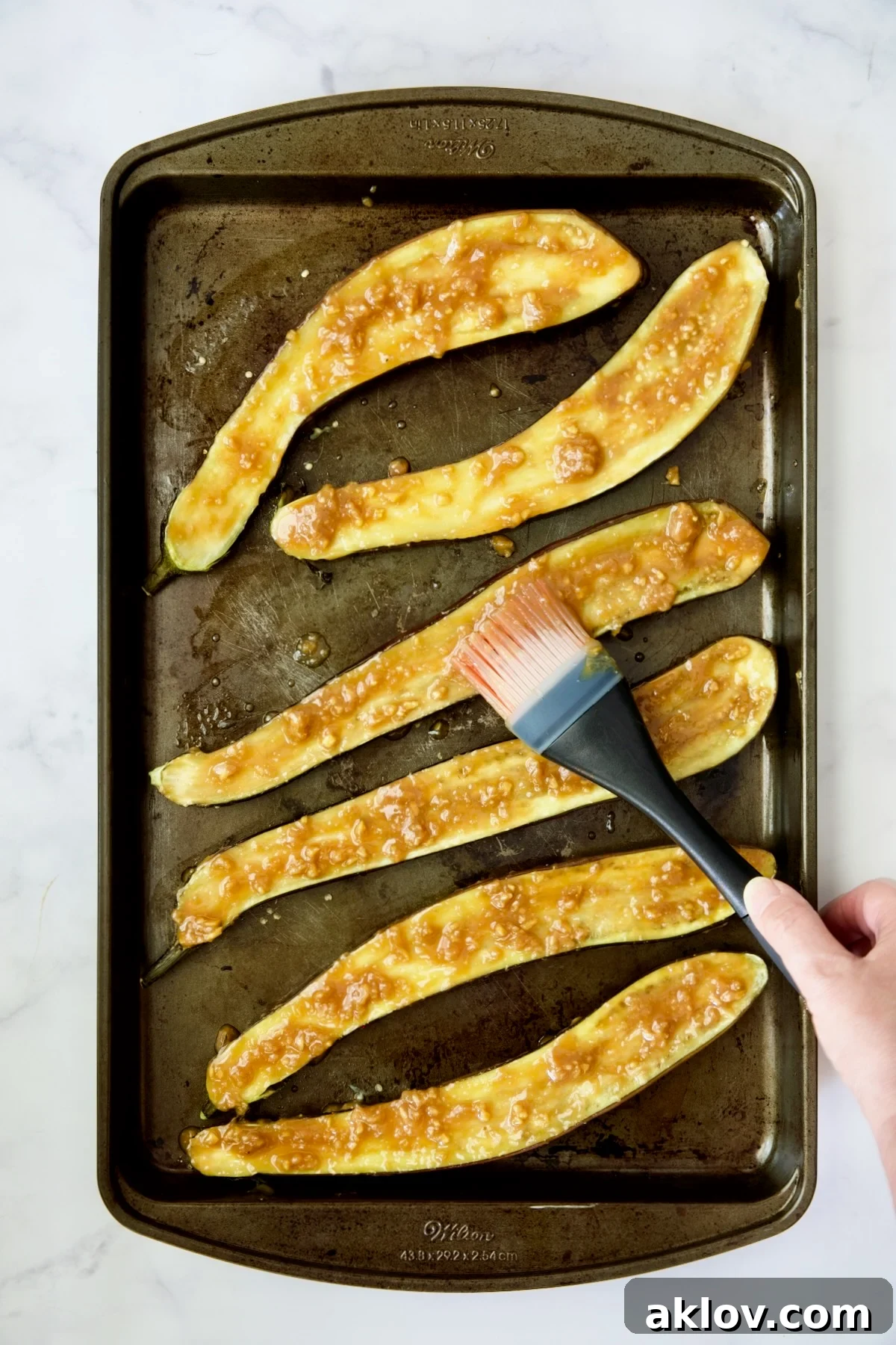 Six baked Japanese eggplant halves on a baking sheet, being meticulously brushed with the thick, glossy miso glaze.