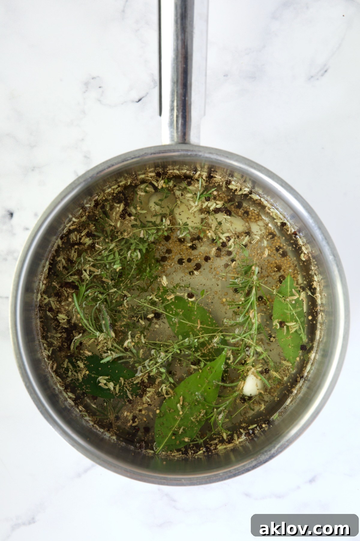 The pickling brine for Giardiniera simmering in a stainless steel saucepan, with herbs and spices visible.