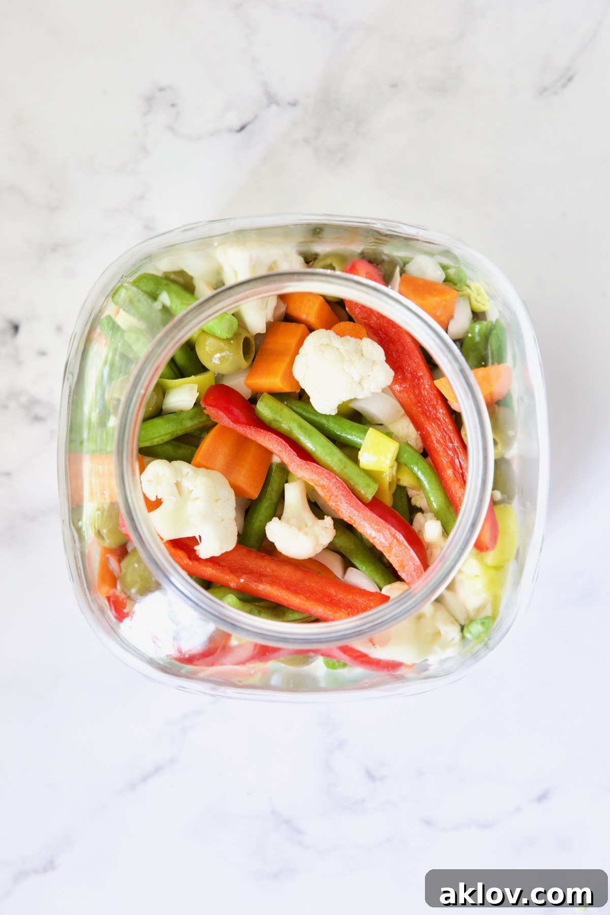 Assorted Giardiniera vegetables, including cauliflower, carrots, and green beans, carefully layered in a large glass jar before the brine is added.