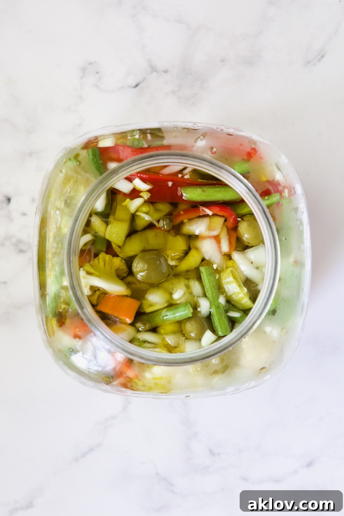 Hot brine being poured over the Giardiniera vegetables in a glass jar, showing them becoming submerged and starting the pickling process.