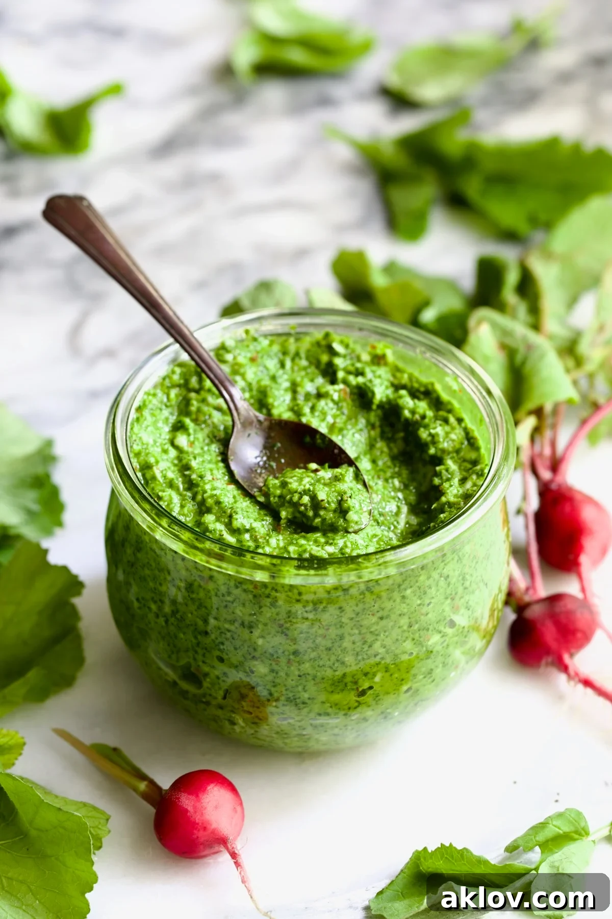 Radish Greens Pesto in glass jar with radish greens scattered around it.