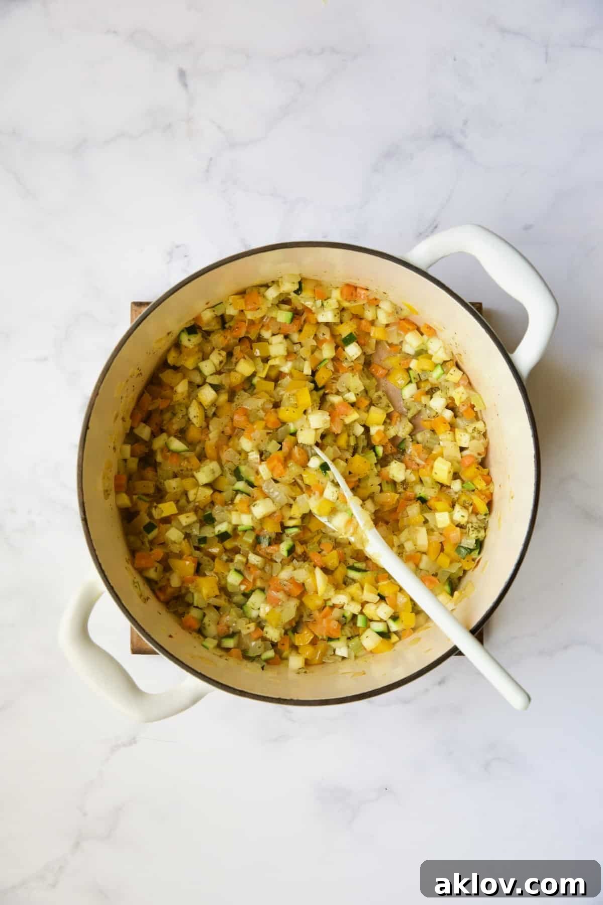 Cooked vegetables with Italian seasoning in white Dutch oven.