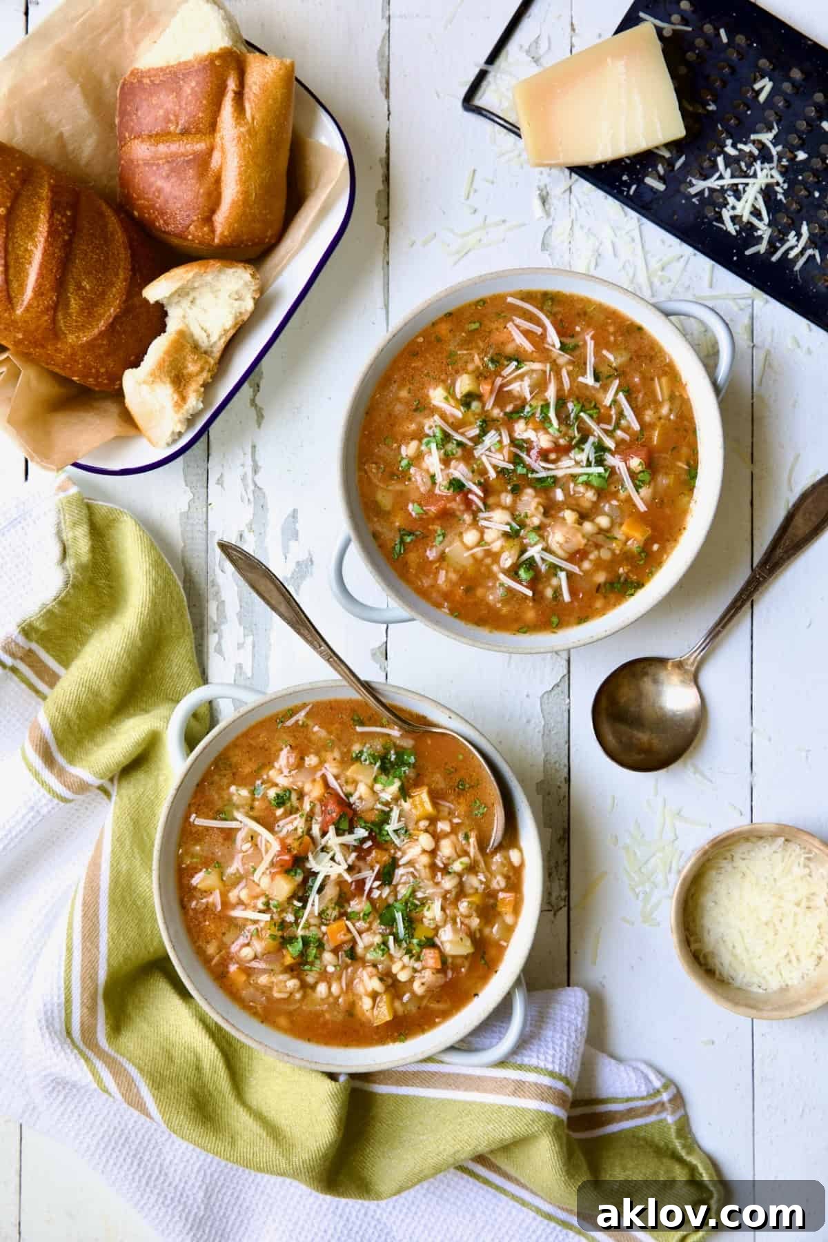 Two bowls of Vegetable Barley Soup on white distressed background with bread and cheese.