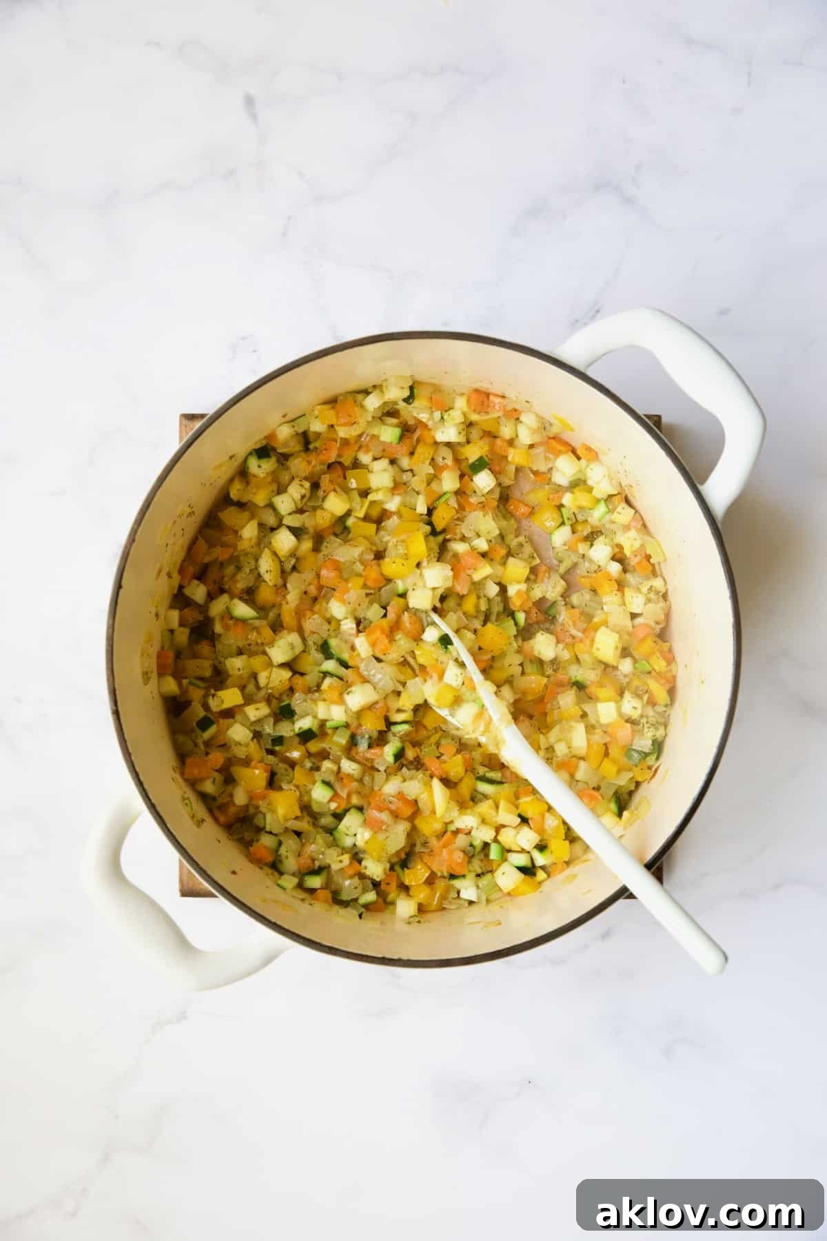 Cooked diced vegetables in white Dutch oven with white mixing spoon.