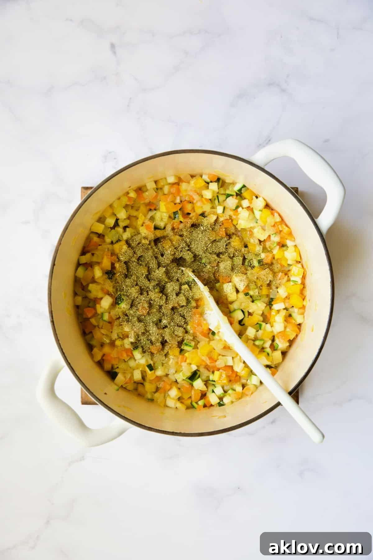 Cooked vegetables in white Dutch oven with Italian seasoning added about to be stirred.