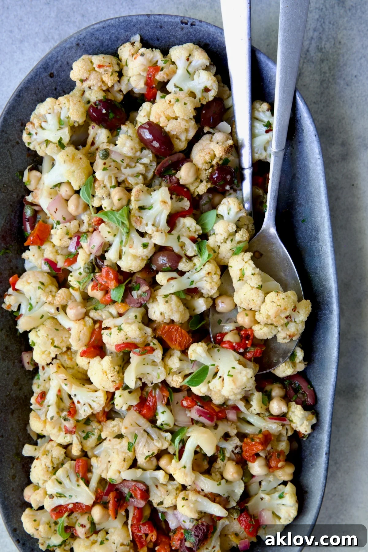 A beautiful warm Roasted Cauliflower Salad served on a gray speckled platter with elegant serving utensils, ready to be enjoyed.