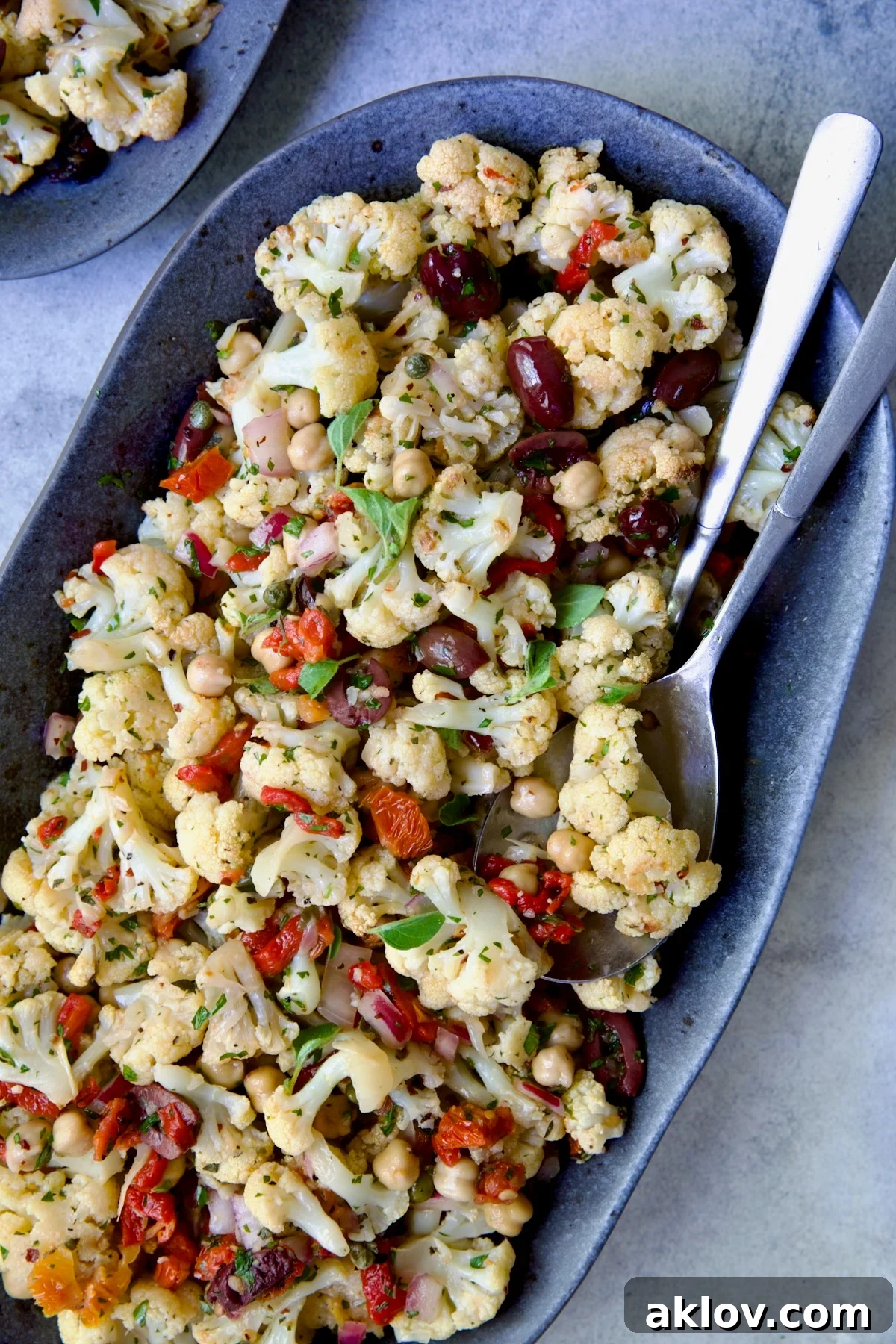 The complete Roasted Cauliflower Salad on a gray speckled platter with serving utensils, ready for a delicious meal.