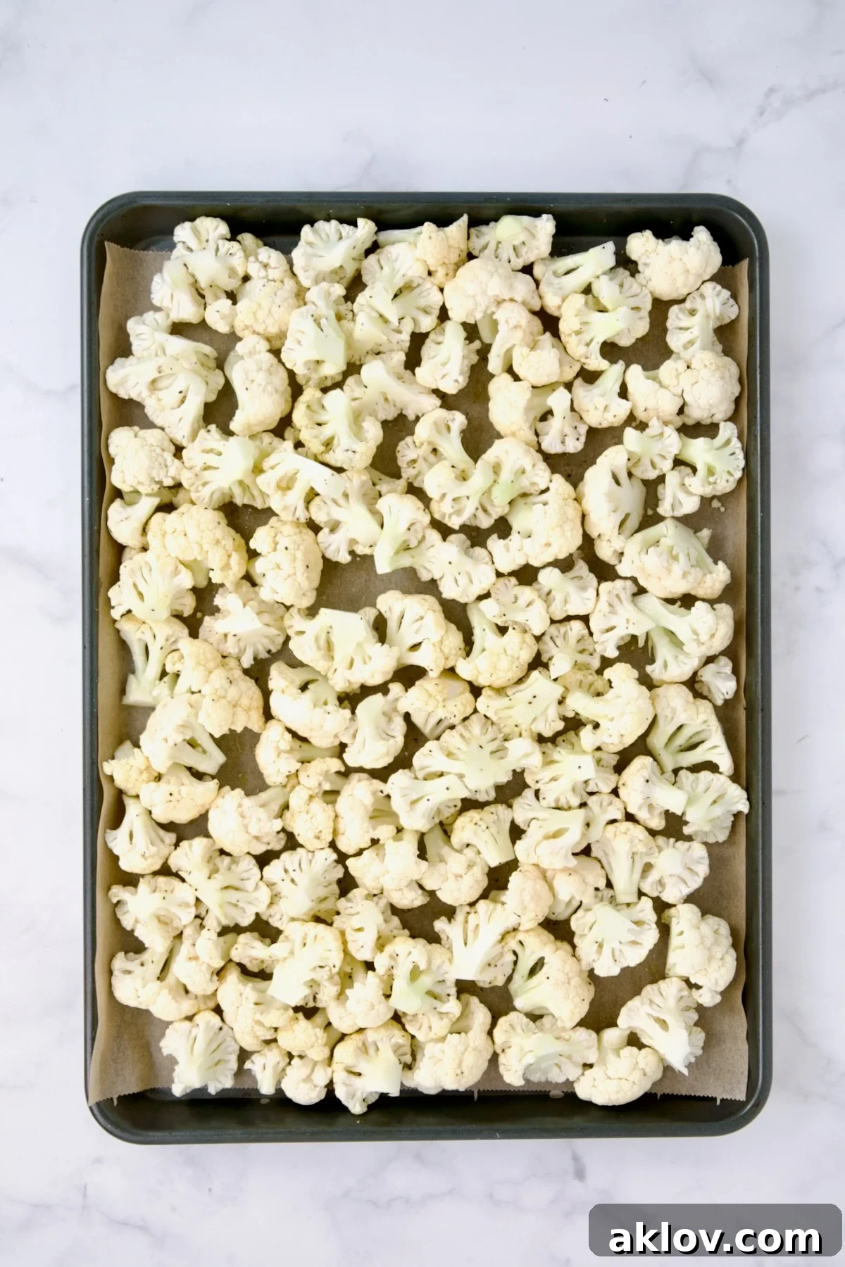 Uncooked cauliflower florets spread out on a parchment paper-lined baking sheet, ready for roasting.
