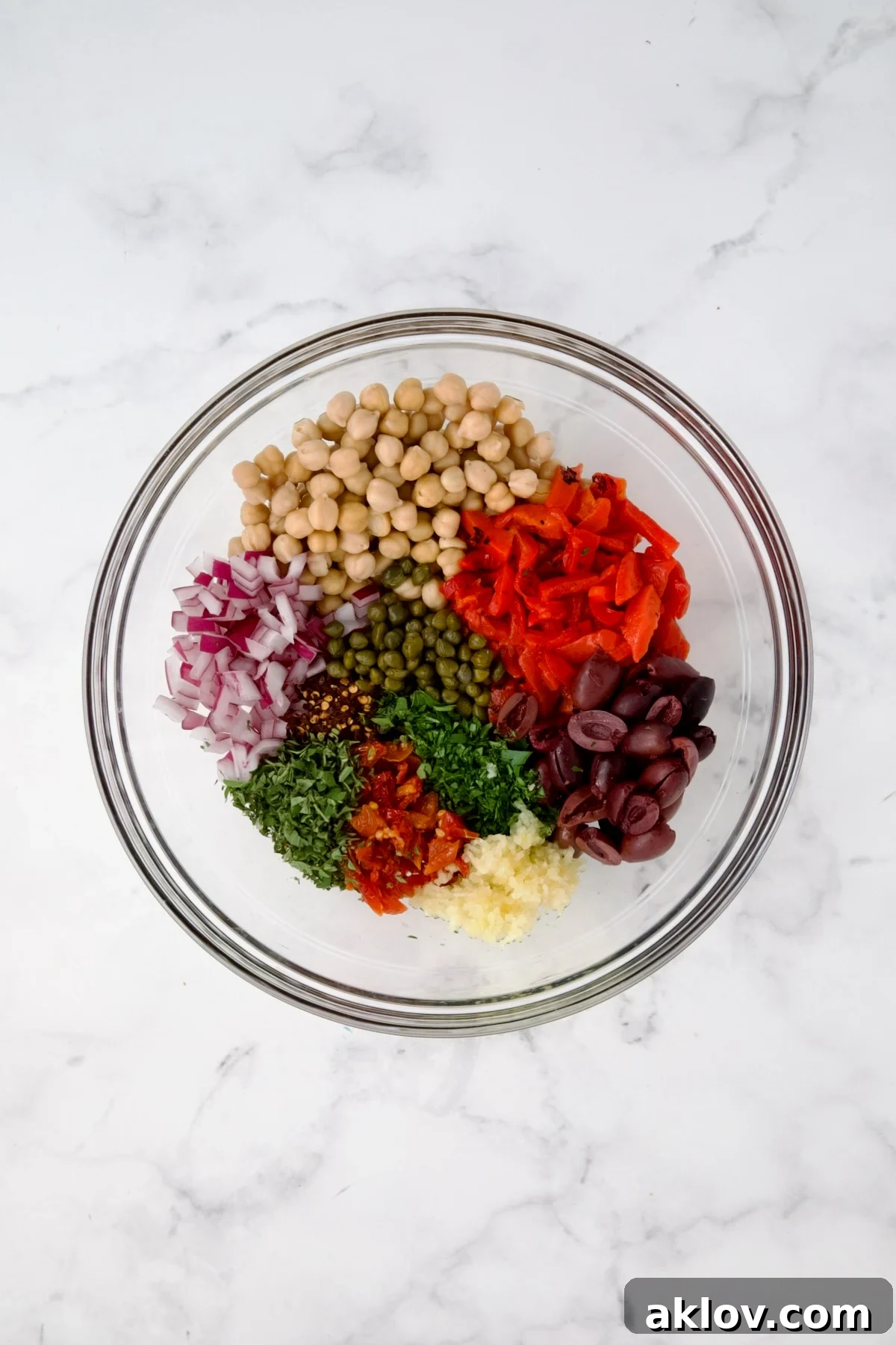 Various prepped ingredients for the cauliflower salad, including chickpeas, olives, and herbs, in a glass bowl before being combined.
