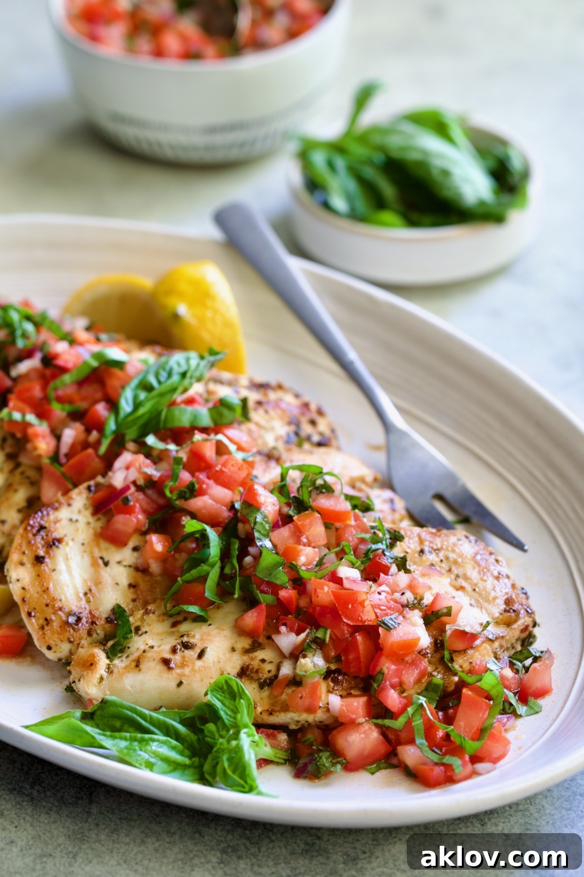 Chicken Bruschetta on oval white platter garnished with fresh lemons and basil.