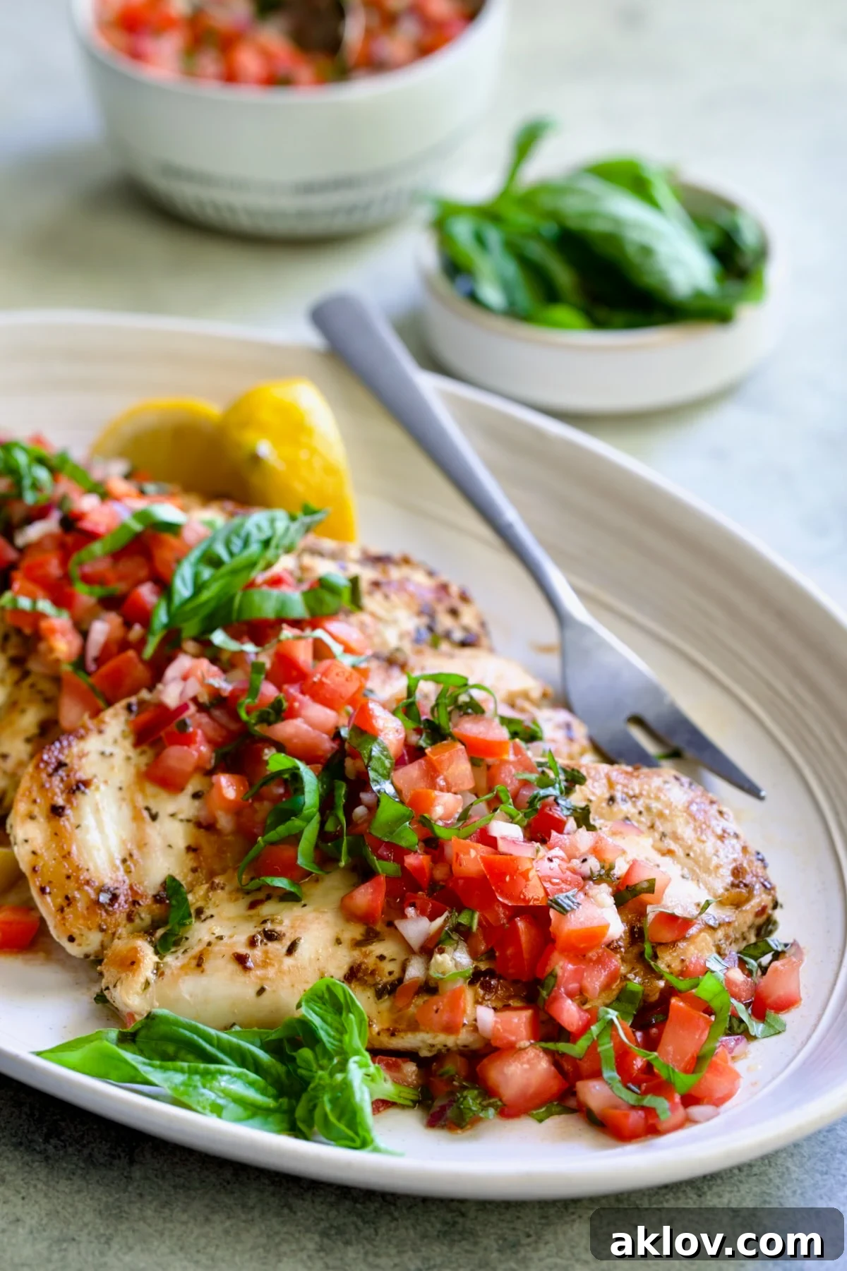 Chicken Bruschetta on oval white platter garnished with fresh lemons and basil.