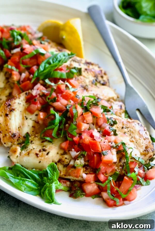Chicken Bruschetta on oval white platter garnished with fresh lemons and basil.