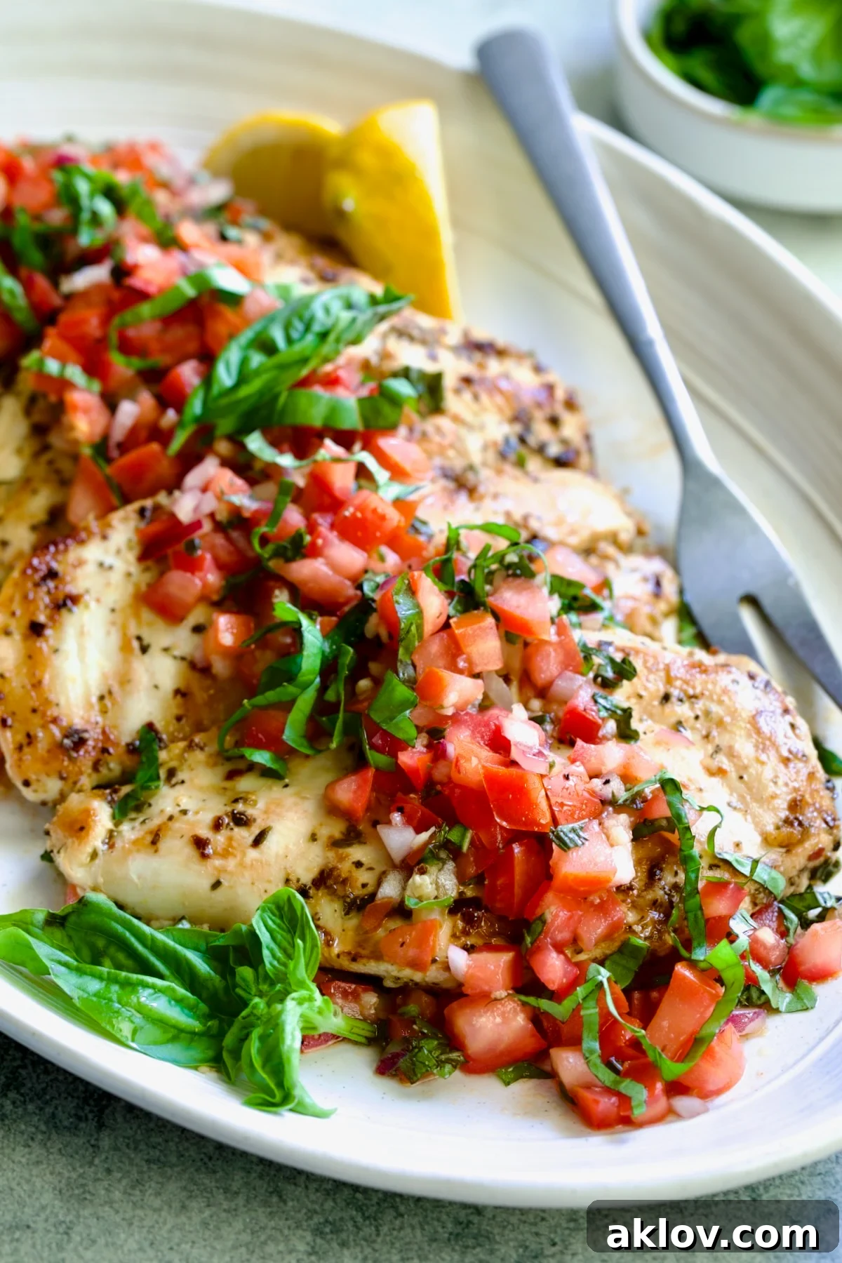 Chicken Bruschetta on oval white platter garnished with fresh lemons and basil.