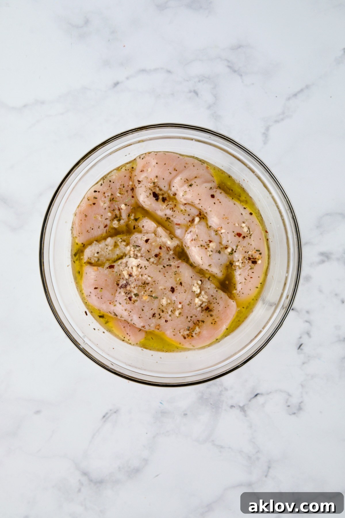 Chicken cutlets in marinade in glass bowl.
