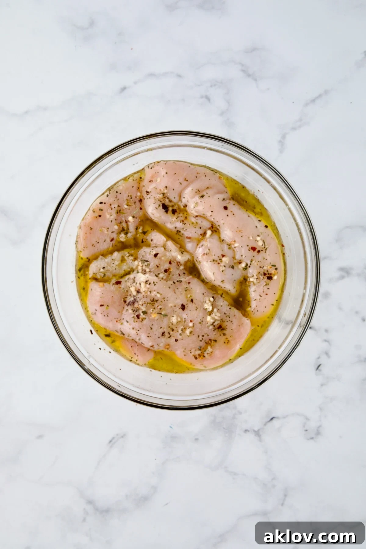 Chicken cutlets in marinade in glass bowl.