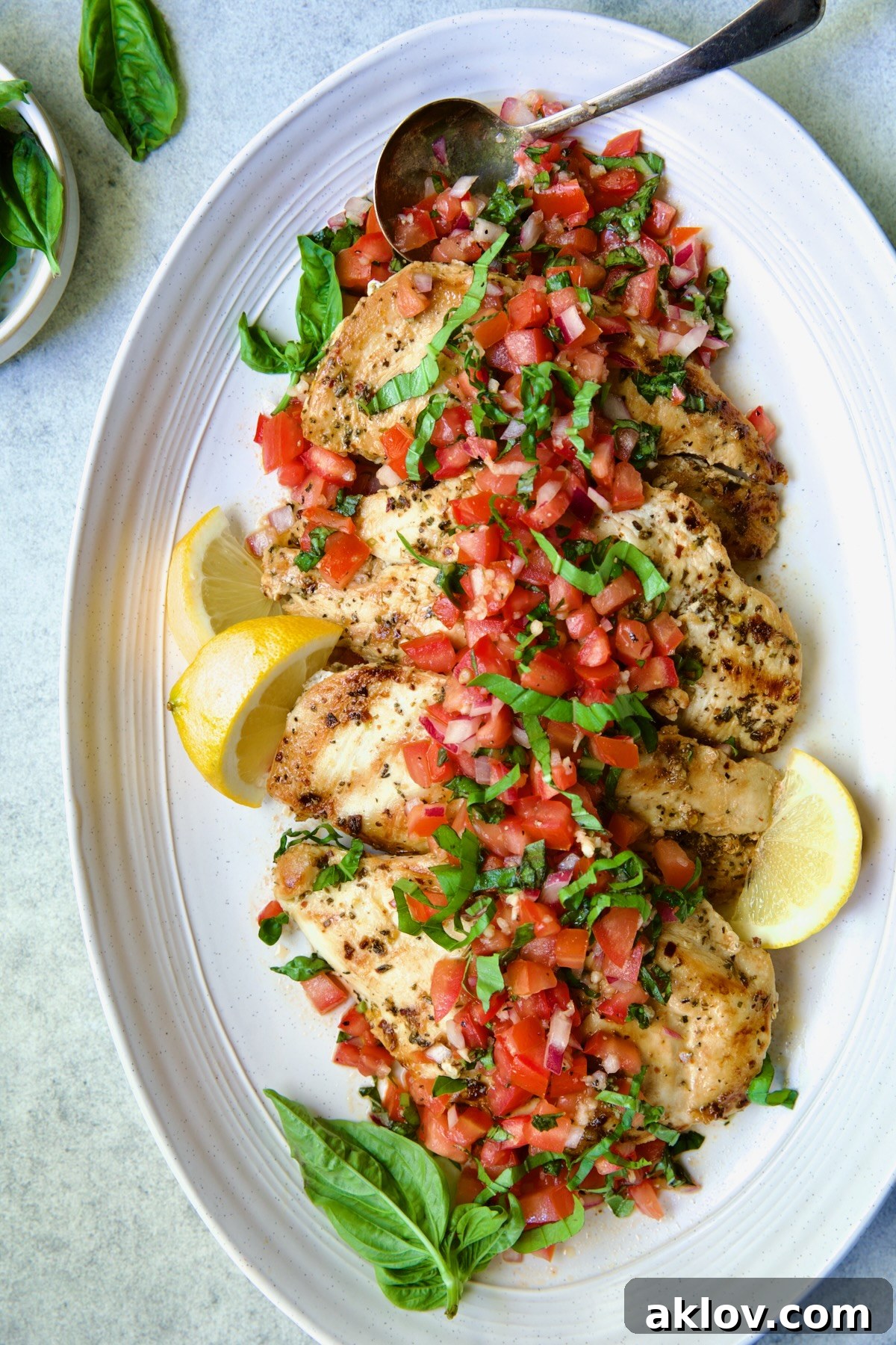 Chicken Bruschetta on oval white platter garnished with fresh lemons and basil.