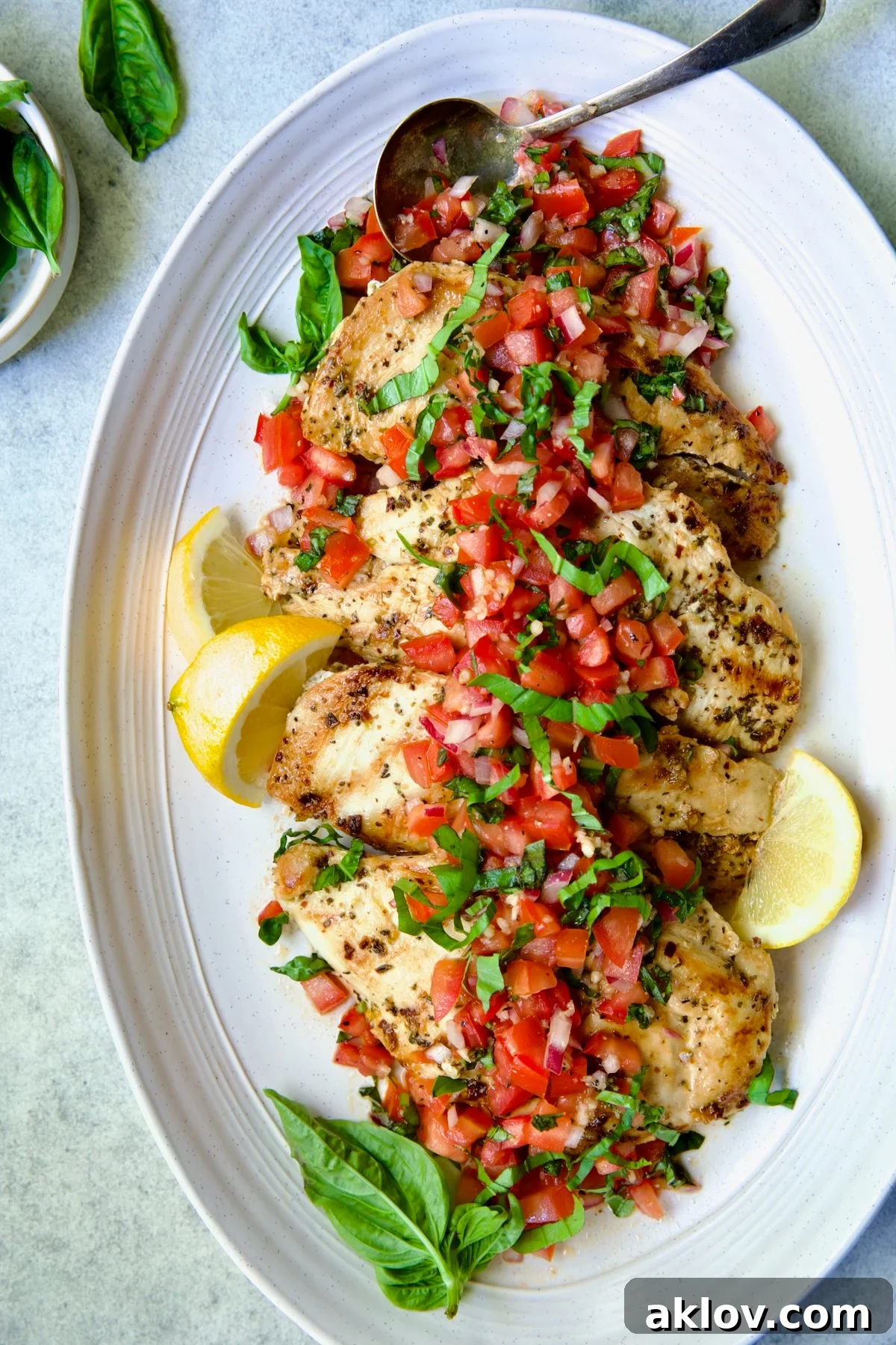 Chicken Bruschetta on oval white platter garnished with fresh lemons and basil.