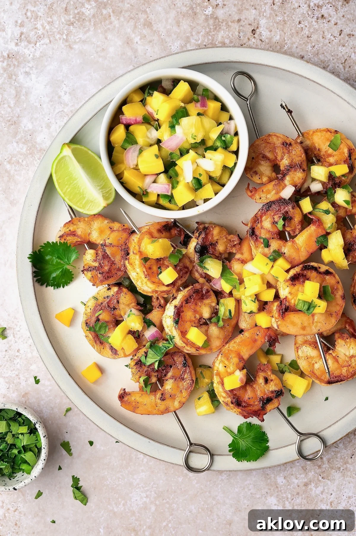 Exquisitely grilled shrimp skewers served alongside a vibrant mango pineapple salsa on a pristine white plate.