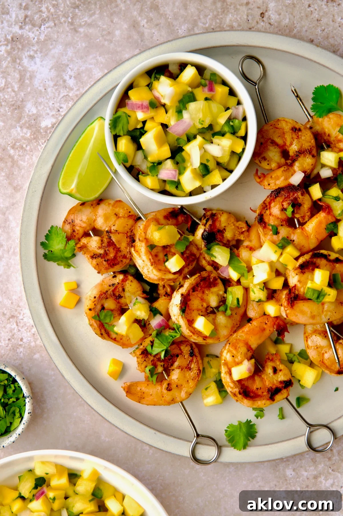 A close-up shot of grilled shrimp skewers presented on a round white plate, beautifully garnished with fresh mango pineapple salsa.