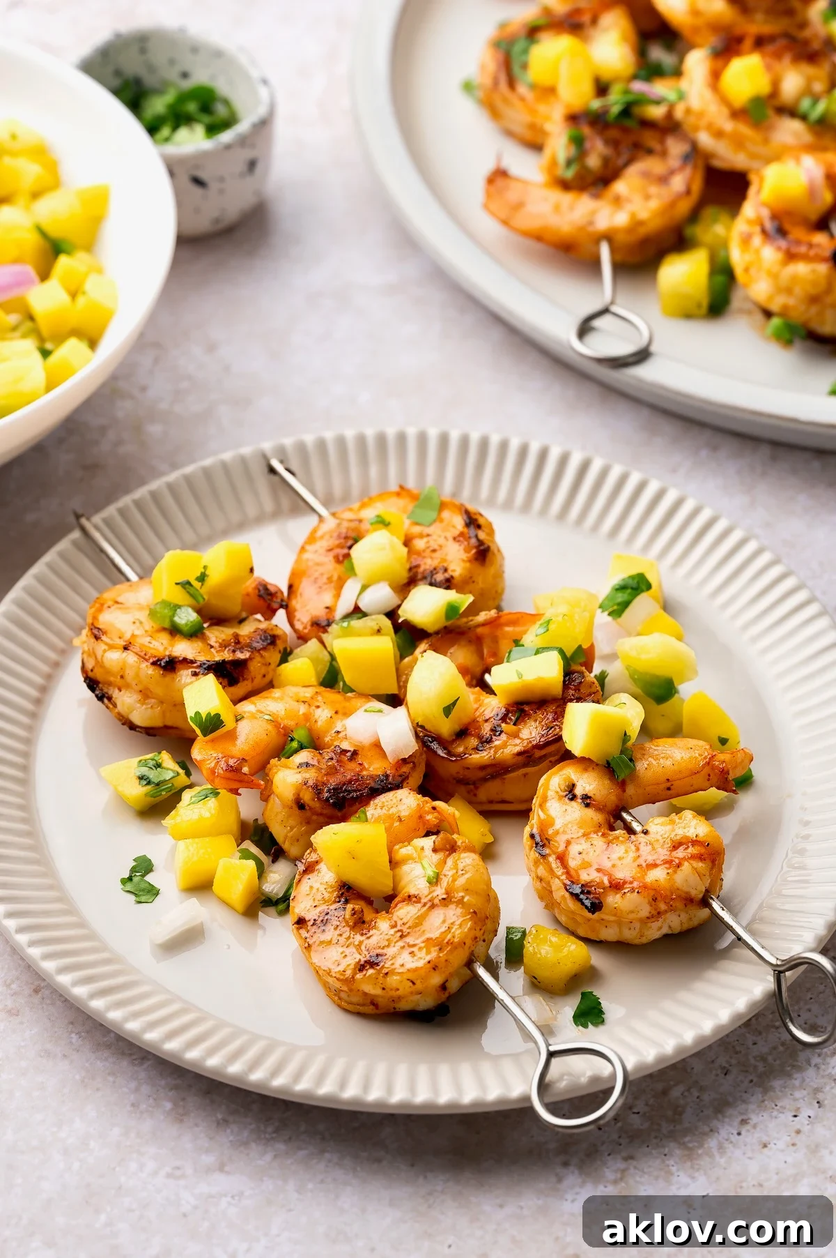 Two grilled shrimp skewers served with mango pineapple salsa on a small, elegant round white plate, highlighting a perfect summer meal.
