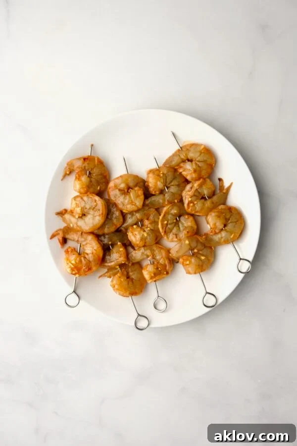 Raw, marinated shrimp expertly threaded onto skewers, arranged on a white plate, awaiting the grill.