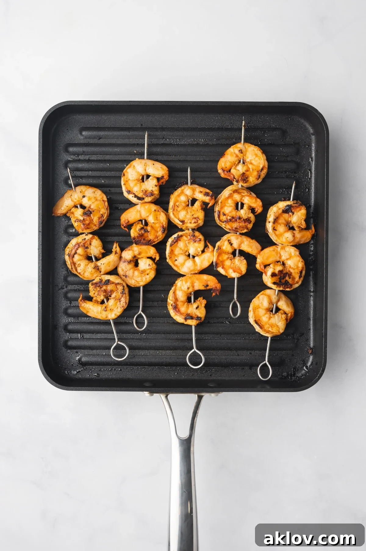 Perfectly grilled shrimp skewers cooking on a square grill pan, showing off their beautiful char.