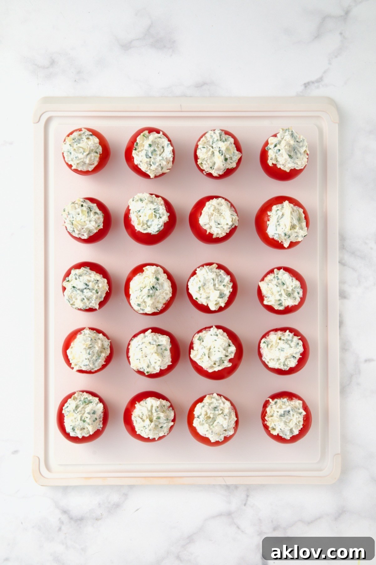 20 stuffed Campari tomatoes on white plastic cutting board.