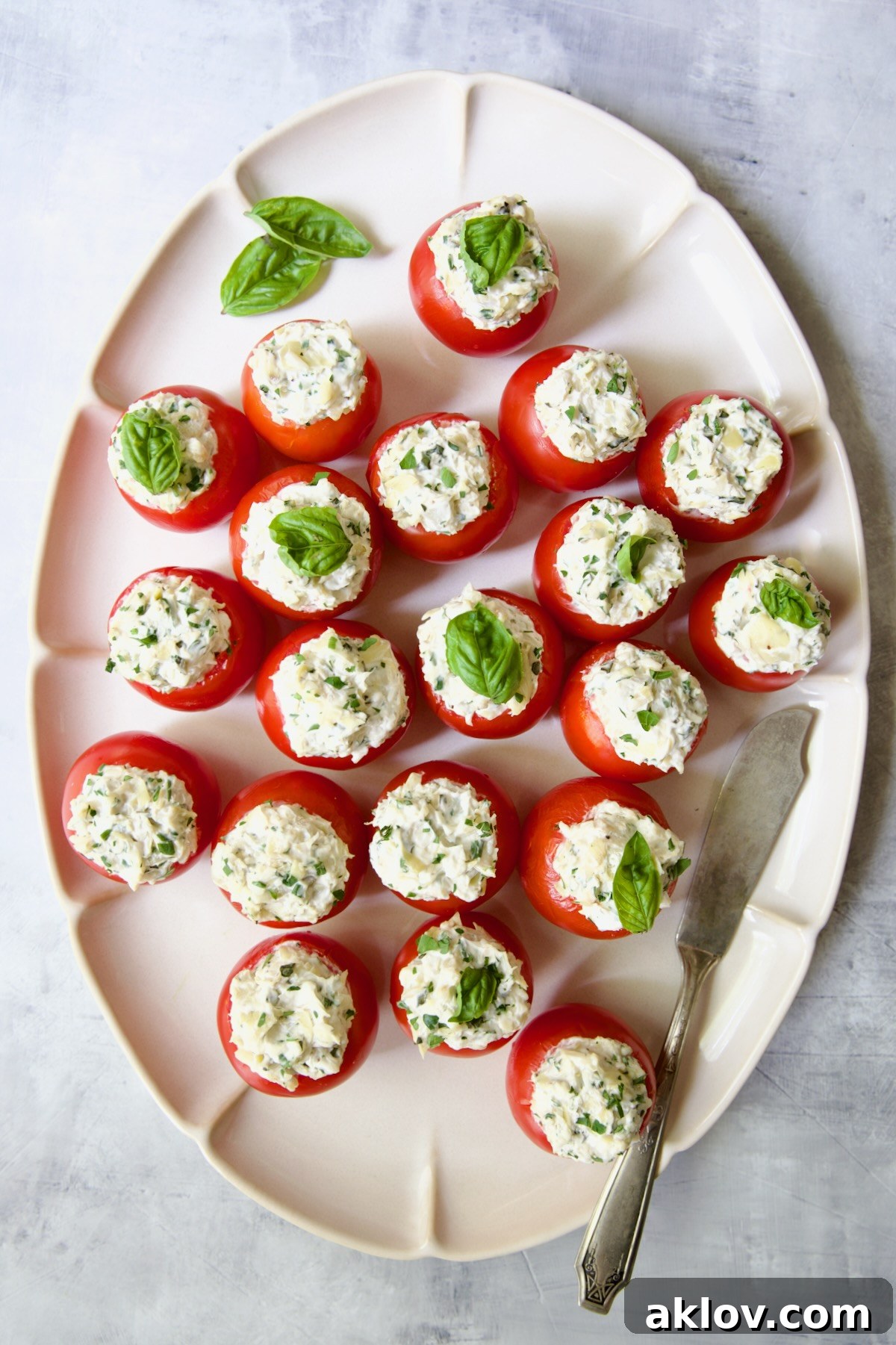 Cream Cheese and Artichoke Stuffed Tomatoes on oval white platter garnished with fresh basil leaves.