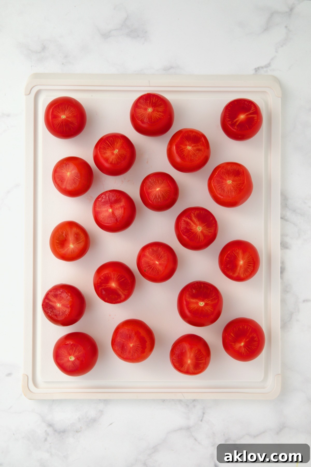 Campari tomatoes on white plastic cutting board with tops sliced off.