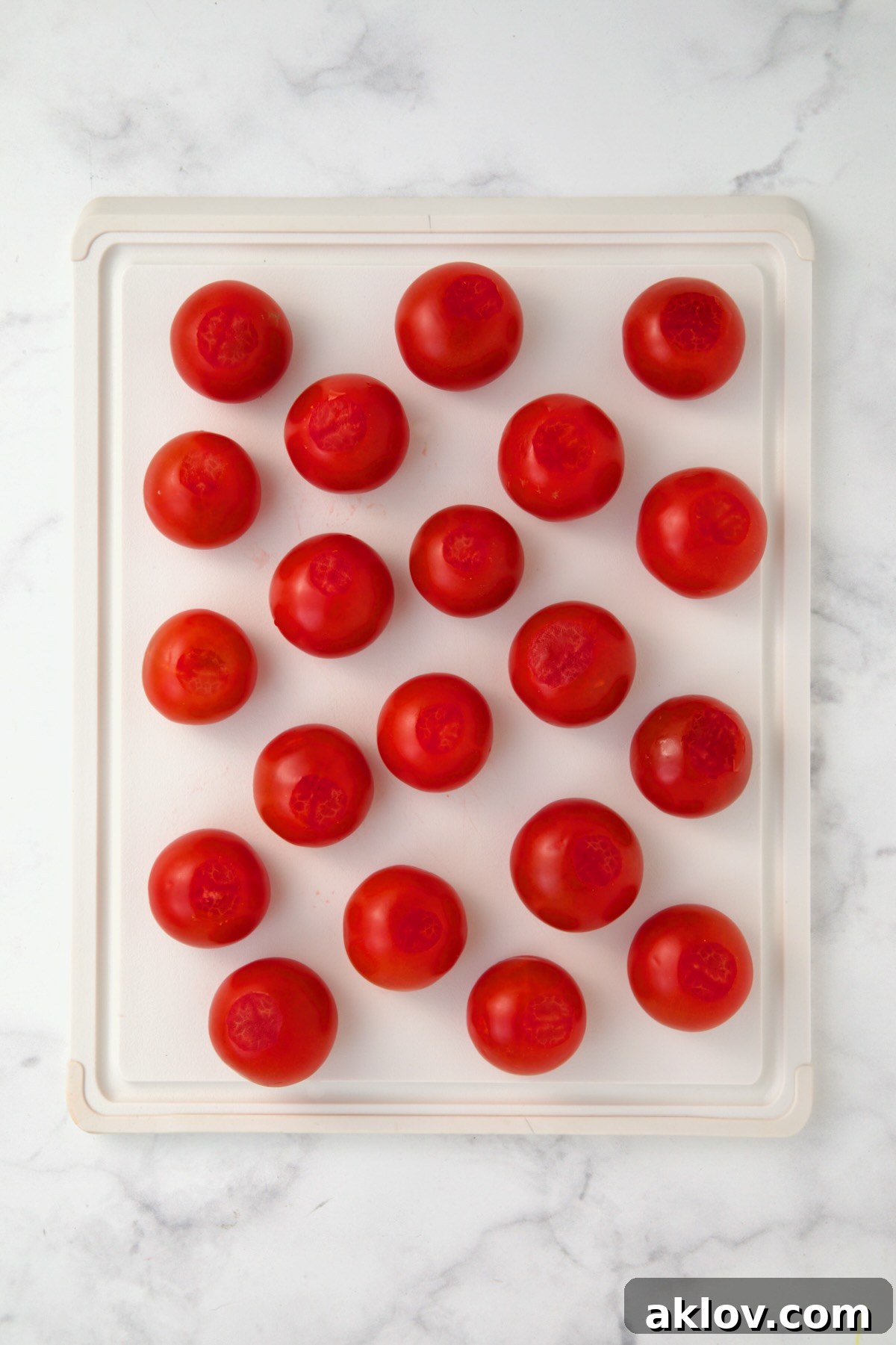 Campari tomatoes on white plastic cutting board with bottoms sliced off.