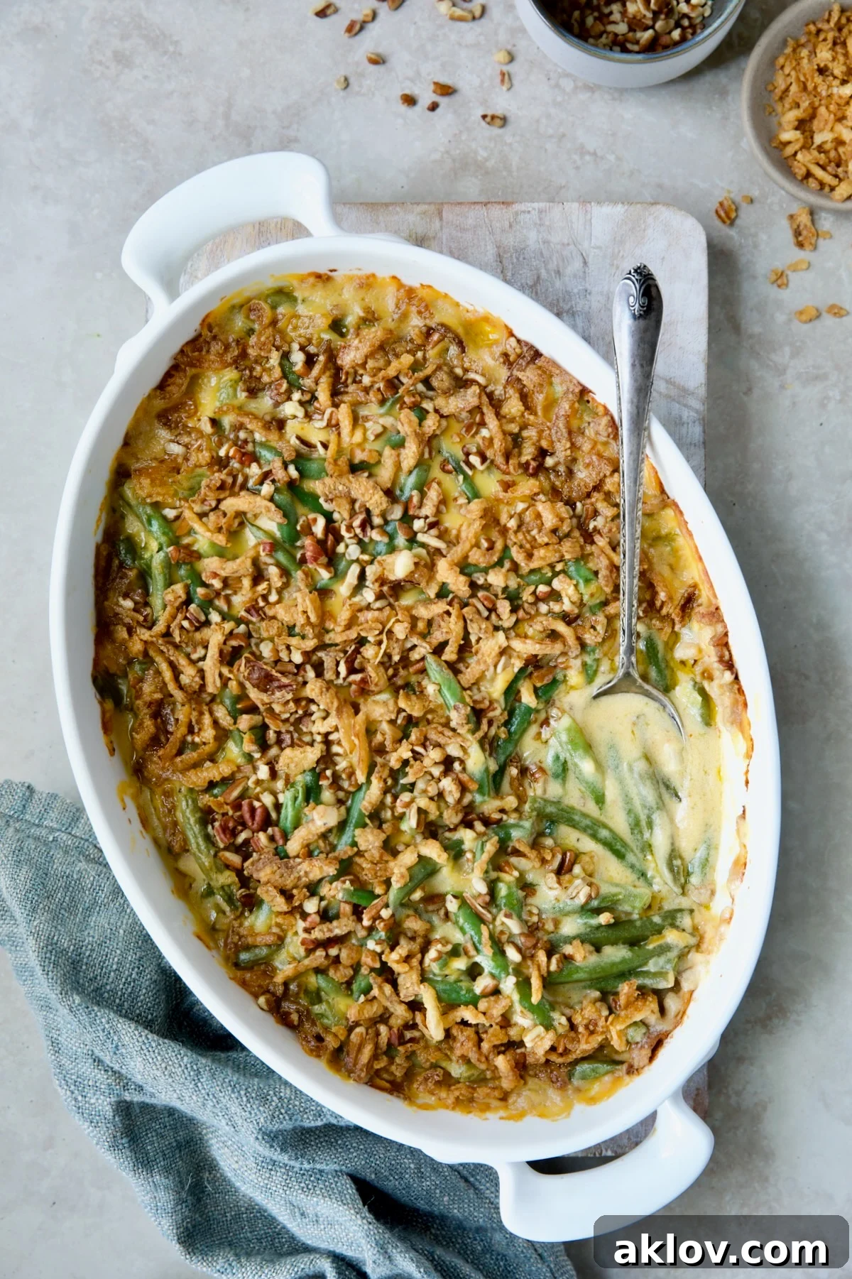 Delightful Cheesy Green Bean Casserole in an elegant white oval gratin dish, ready to be served, accompanied by a silver serving spoon and a blue linen napkin.